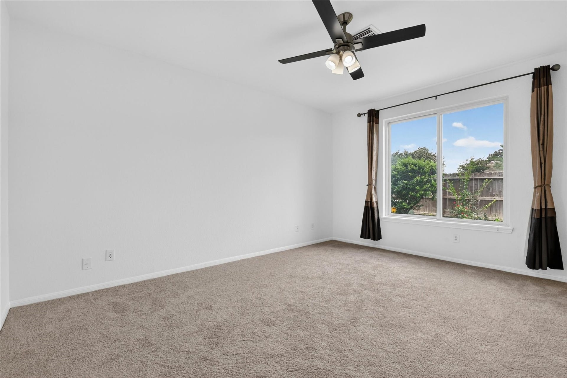 4610 Misty Morning Court, Missouri City, TX 77459 This bedroom features a carpeted floor, neutral walls, and a ceiling fan with lights. A large window offers natural light and a view of the backyard.