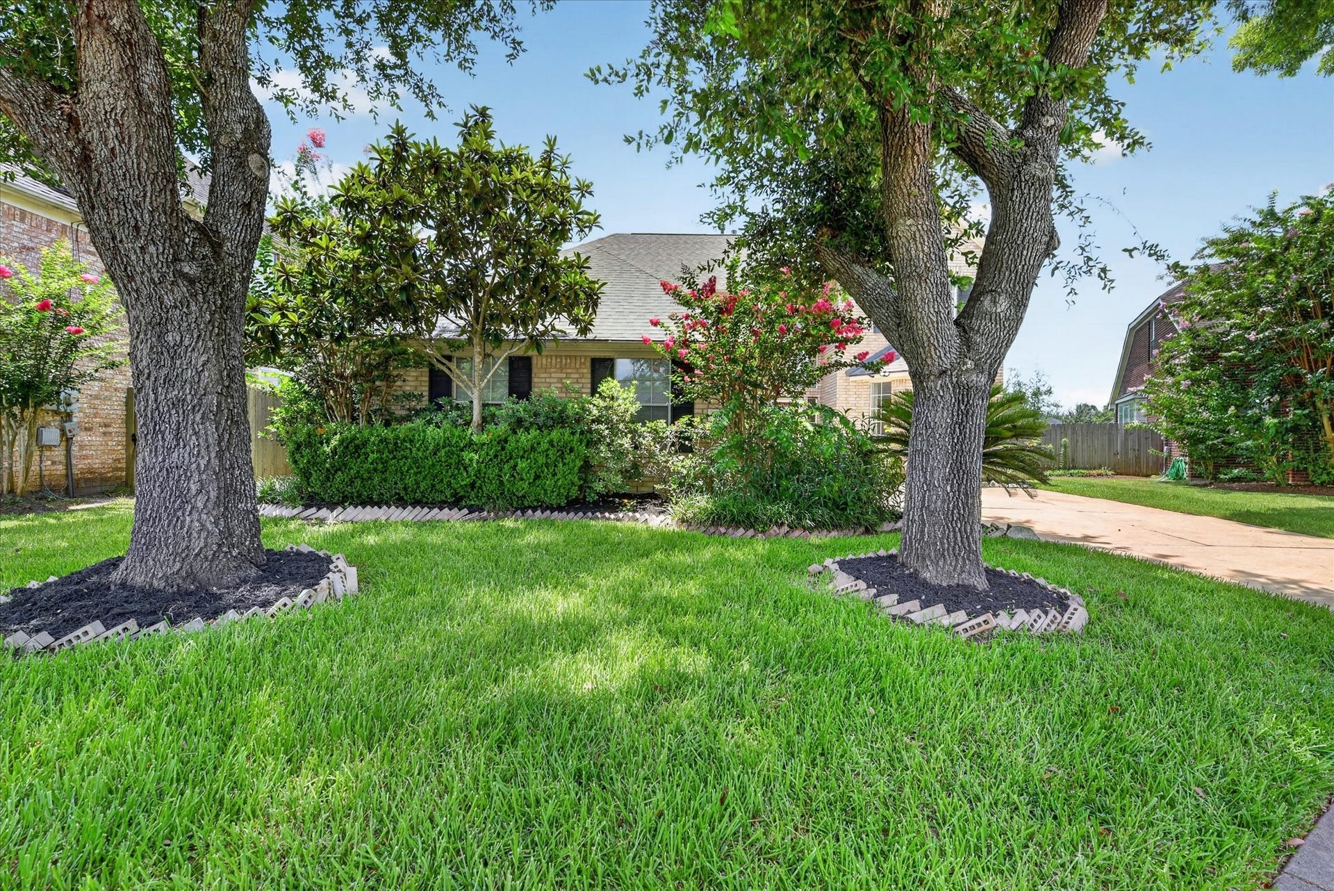 4610 Misty Morning Court, Missouri City, TX 77459 Charming front yard featuring lush green grass, mature trees, and well-maintained landscaping with flowering shrubs. The brick facade of the house is partially visible, creating a welcoming entrance.