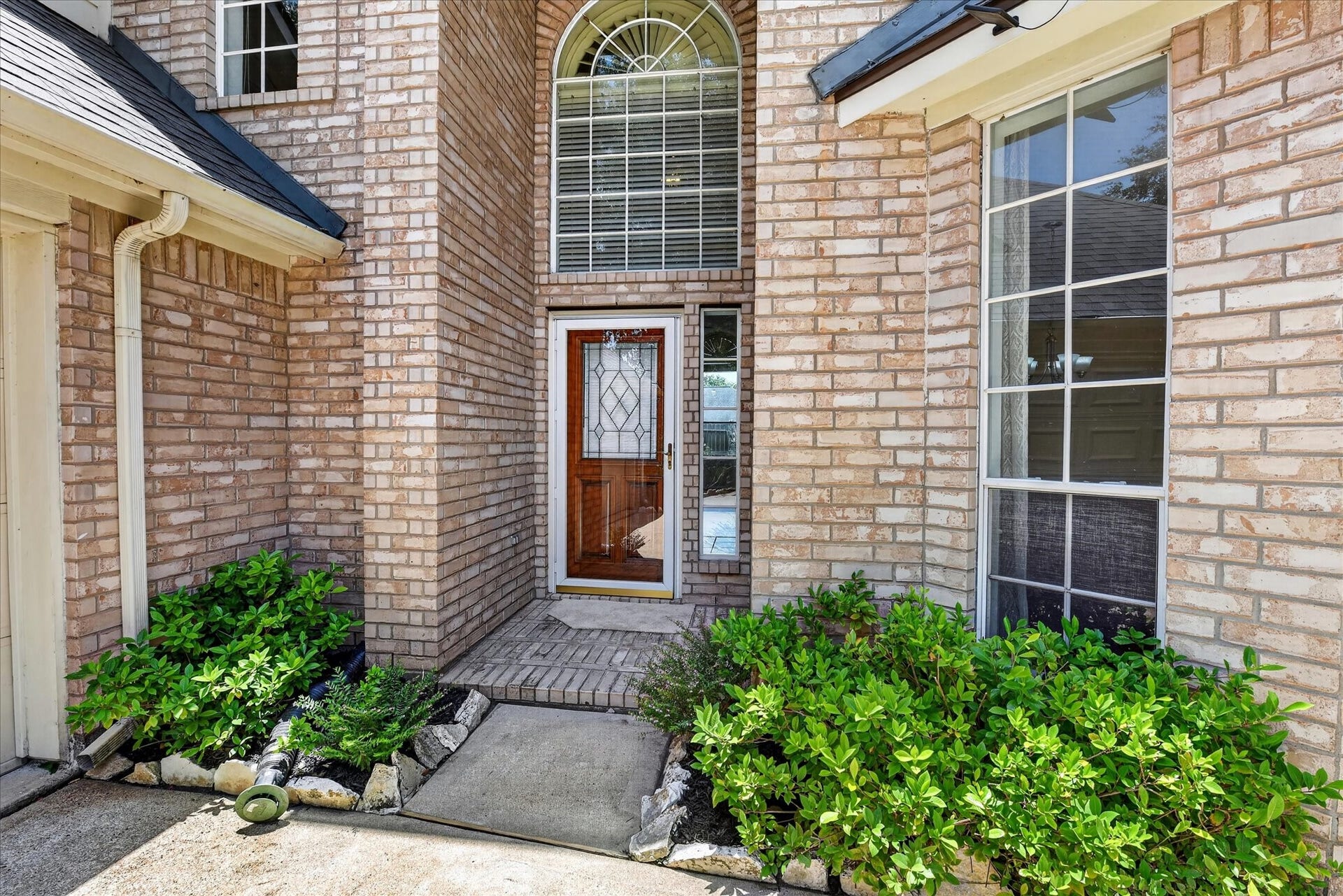 4610 Misty Morning Court, Missouri City, TX 77459 This photo showcases a welcoming brick entryway with a wooden door featuring decorative glass. The area is framed by well-maintained shrubs and features an arched window above, adding elegance and natural light.