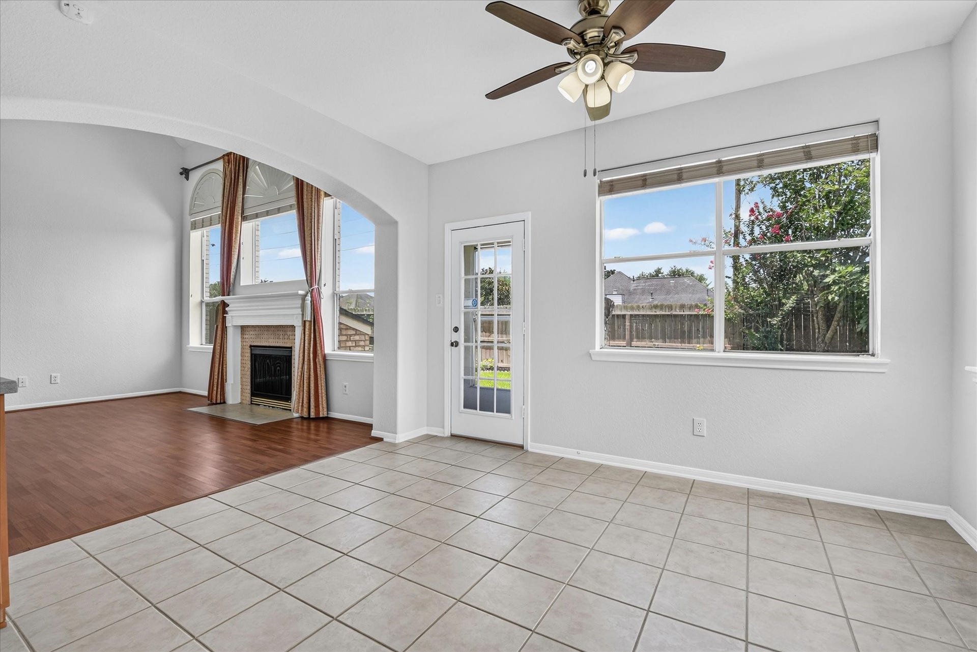 4610 Misty Morning Court, Missouri City, TX 77459 This bright living space features a tiled floor with a ceiling fan, large windows for natural light, and an arched entry to a cozy area with wood flooring and a fireplace. A door leads to a fenced backyard, ideal for outdoor activities.