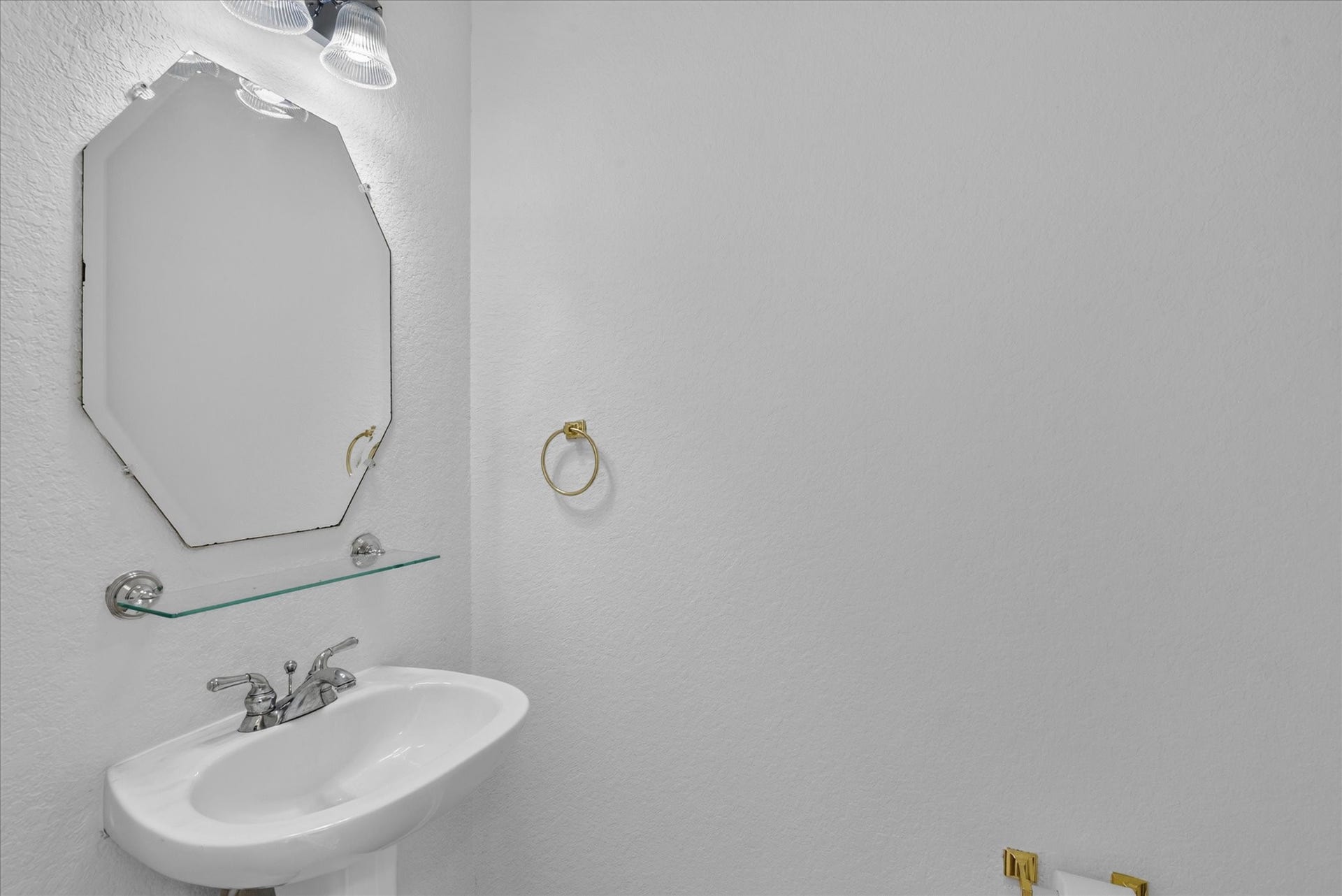 4610 Misty Morning Court, Missouri City, TX 77459 Compact powder room with a white pedestal sink, octagonal mirror, sleek glass shelf, and modern fixtures. Bright, minimal design with ample lighting.