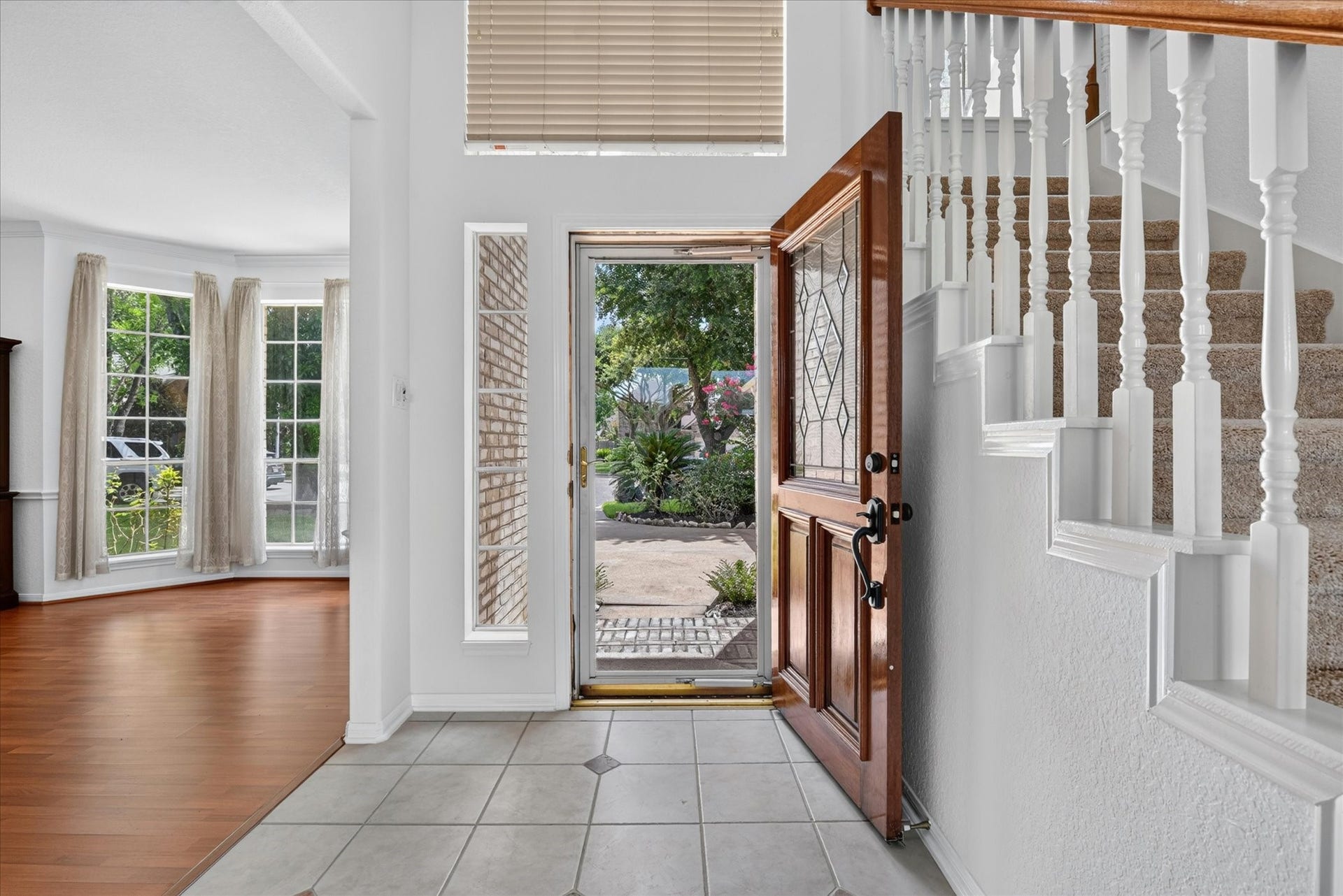 4610 Misty Morning Court, Missouri City, TX 77459 This inviting entryway features a wooden front door with decorative glass, tiled flooring, and a view of the staircase. To the left, a spacious room with large windows and wooden floors offers plenty of natural light, perfect for a living or dining area.