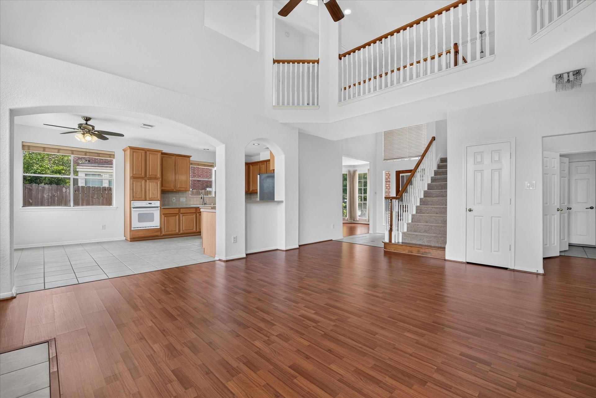4610 Misty Morning Court, Missouri City, TX 77459 This spacious home features an open floor plan with a high ceiling and abundant natural light. The living area boasts elegant wood flooring, leading to a tiled kitchen with wooden cabinetry and modern appliances. A staircase connects to an upper level with a stylish railing, creating a welcoming and airy atmosphere.