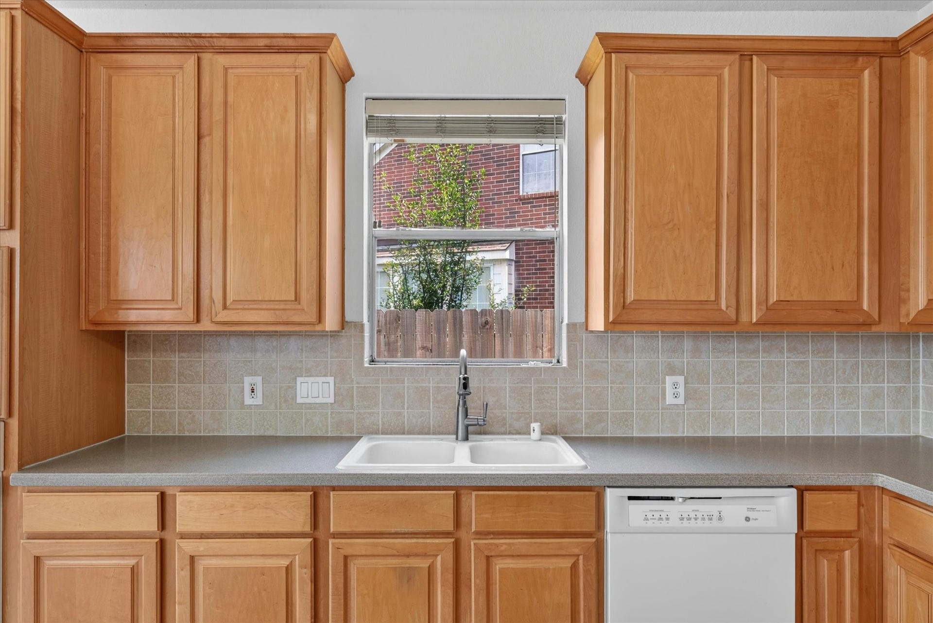 4610 Misty Morning Court, Missouri City, TX 77459 This kitchen features warm wooden cabinets, a sleek countertop, a double sink with a window above, and a built-in dishwasher, offering a functional and inviting space.