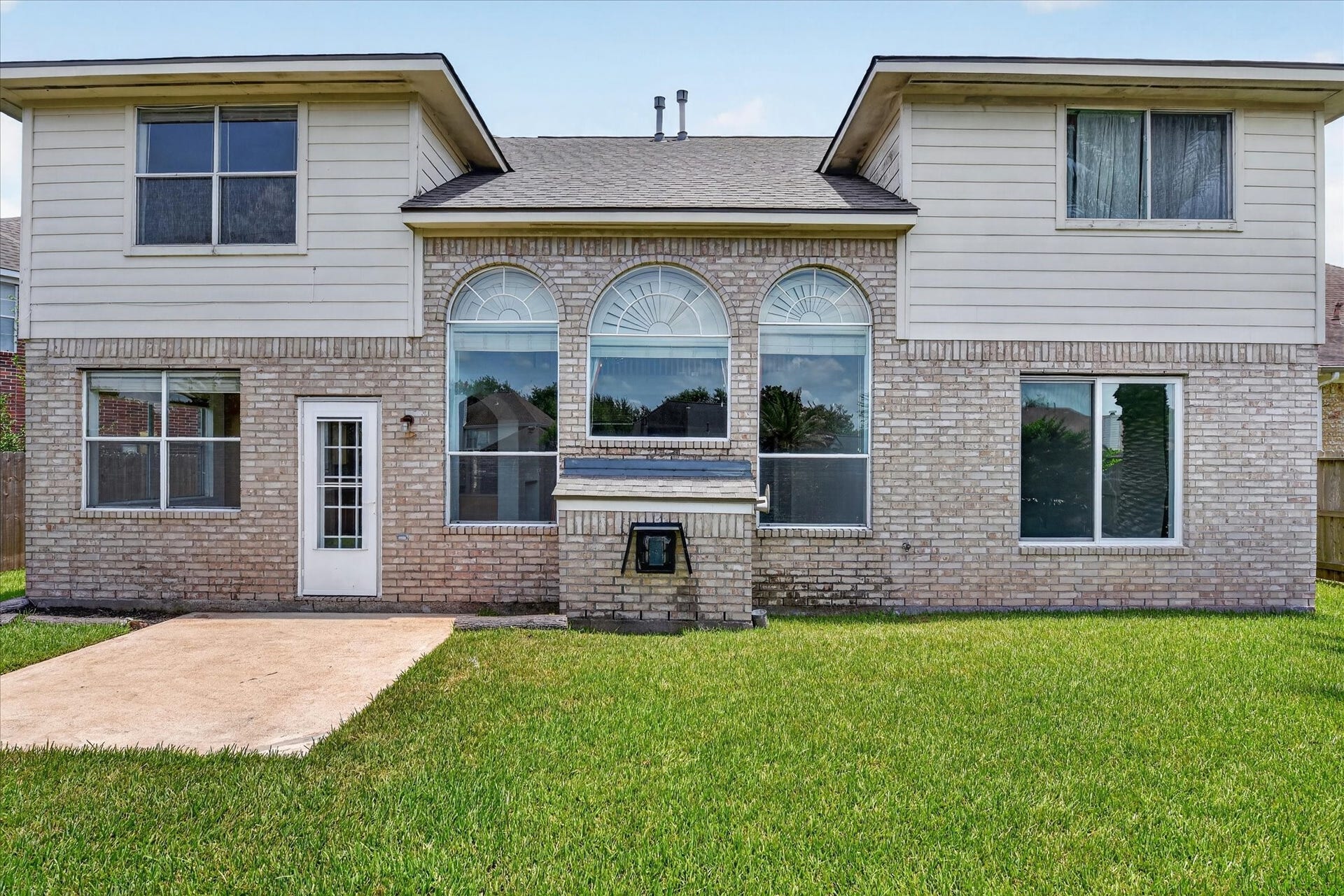 4610 Misty Morning Court, Missouri City, TX 77459 This back view of the spacious two-story home features a charming brick exterior with large arched windows, providing plenty of natural light. It offers a well-maintained lawn and a cozy outdoor patio area, perfect for entertaining or relaxing.