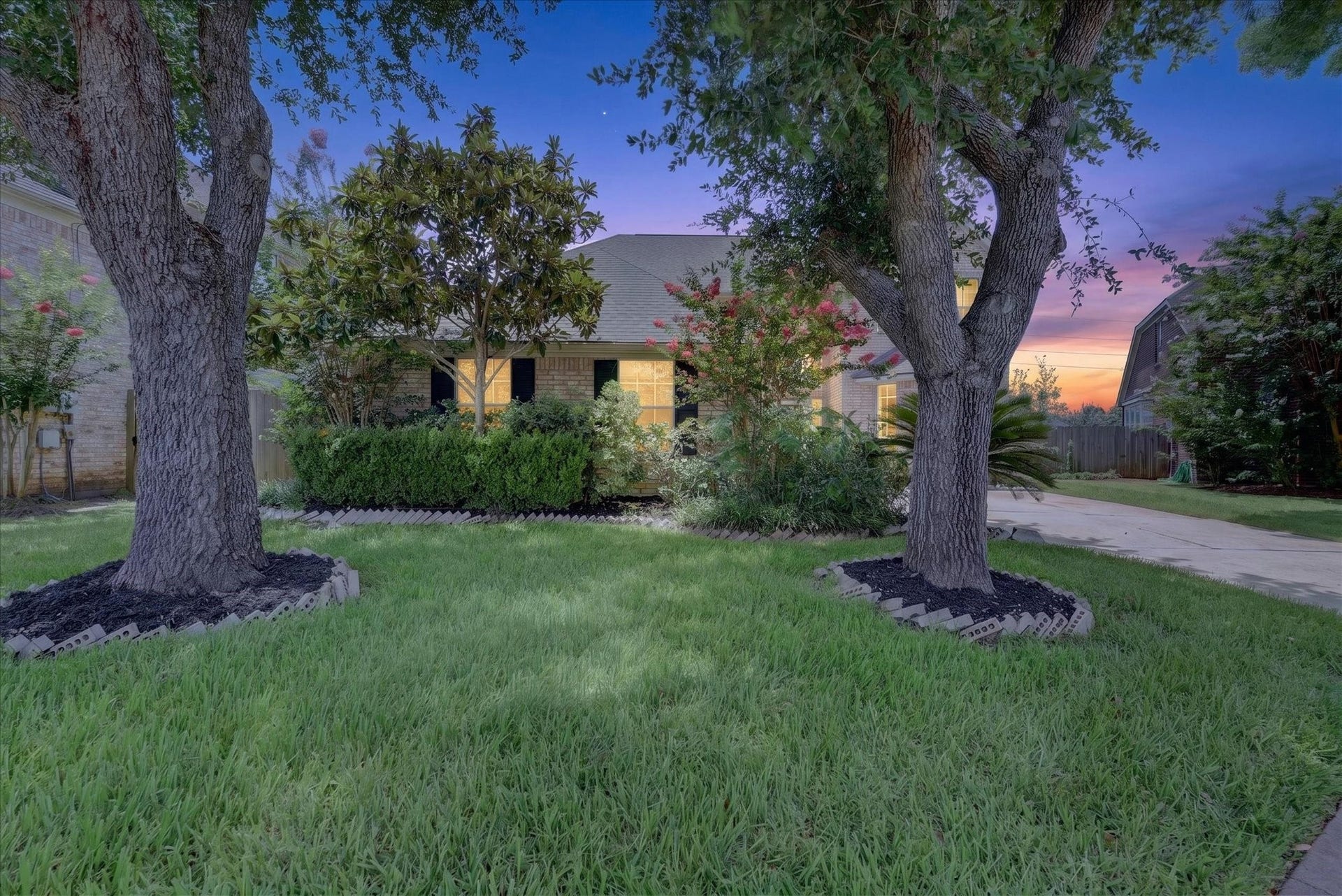 4610 Misty Morning Court, Missouri City, TX 77459 This photo showcases a charming home with a well-maintained front yard featuring lush grass, mature trees, and landscaped shrubs. The driveway leads to a cozy residence, framed by a serene evening sky. Perfect for those seeking a peaceful, inviting atmosphere.