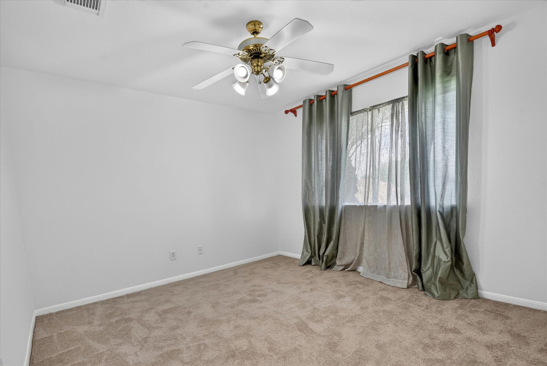 4610 Misty Morning Court, Missouri City, TX 77459 This photo features a bright, bedroom with neutral carpeting and white walls. It has a ceiling fan with a light fixture and a window with green curtains, creating a welcoming atmosphere.