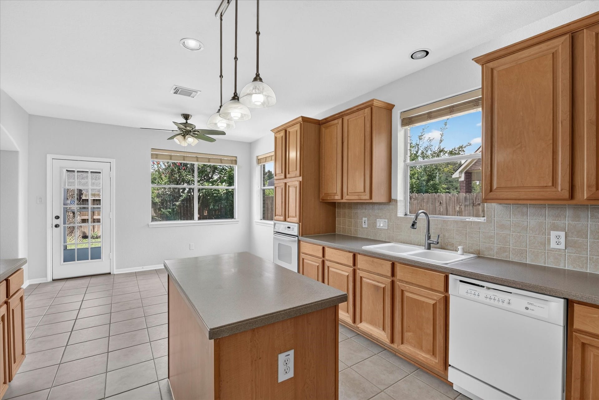 4610 Misty Morning Court, Missouri City, TX 77459 Spacious kitchen with ample natural light, featuring wooden cabinets, a central island, and modern appliances. Tile flooring and a ceiling fan enhance functionality, while large windows and a glass door offer backyard views.