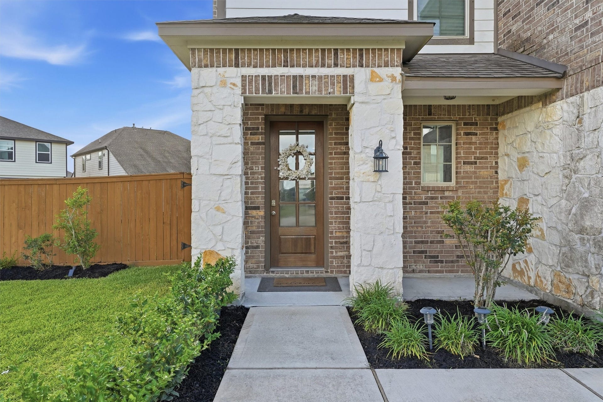 2130 Shellbark Way, La Marque, TX 77568 Inviting front entrance with a mix of brick and stone exterior. Wooden door and the pathway is bordered by neat landscaping. A wooden fence encloses the green lawn, adding privacy and charm.