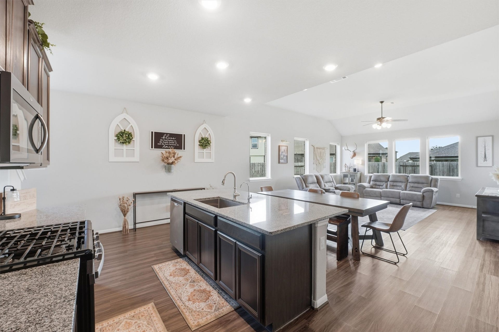 2130 Shellbark Way, La Marque, TX 77568 Open-concept kitchen and living area. The kitchen features modern appliances, a large island with seating, and dark cabinetry. The space transitions smoothly into a cozy living room with ample natural light from multiple windows.