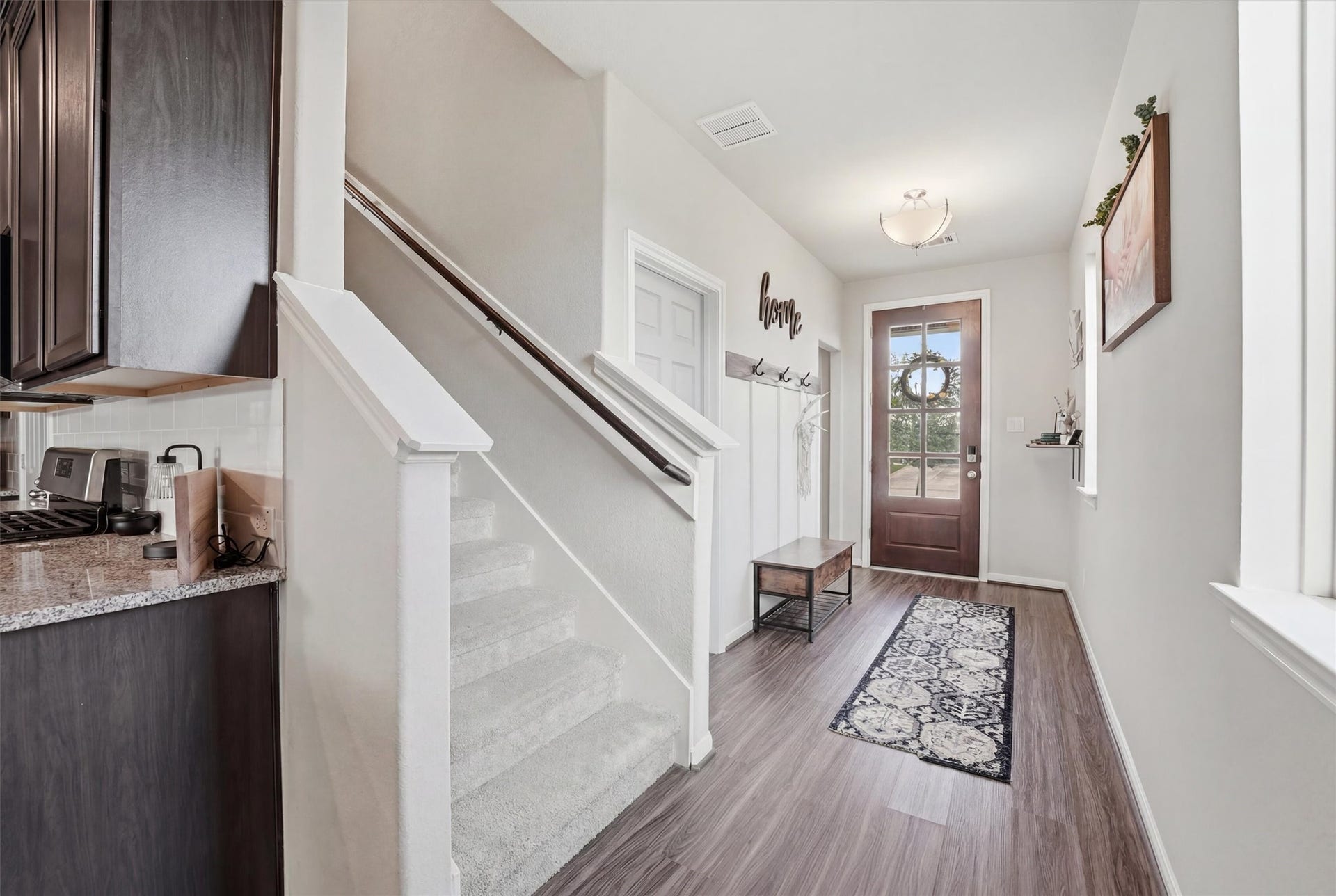 2130 Shellbark Way, La Marque, TX 77568 Welcoming foyer features a wooden front door with glass panels. The staircase leads upstairs, and the adjacent kitchen showcases dark cabinetry and granite countertops, blending functionality with modern elegance.