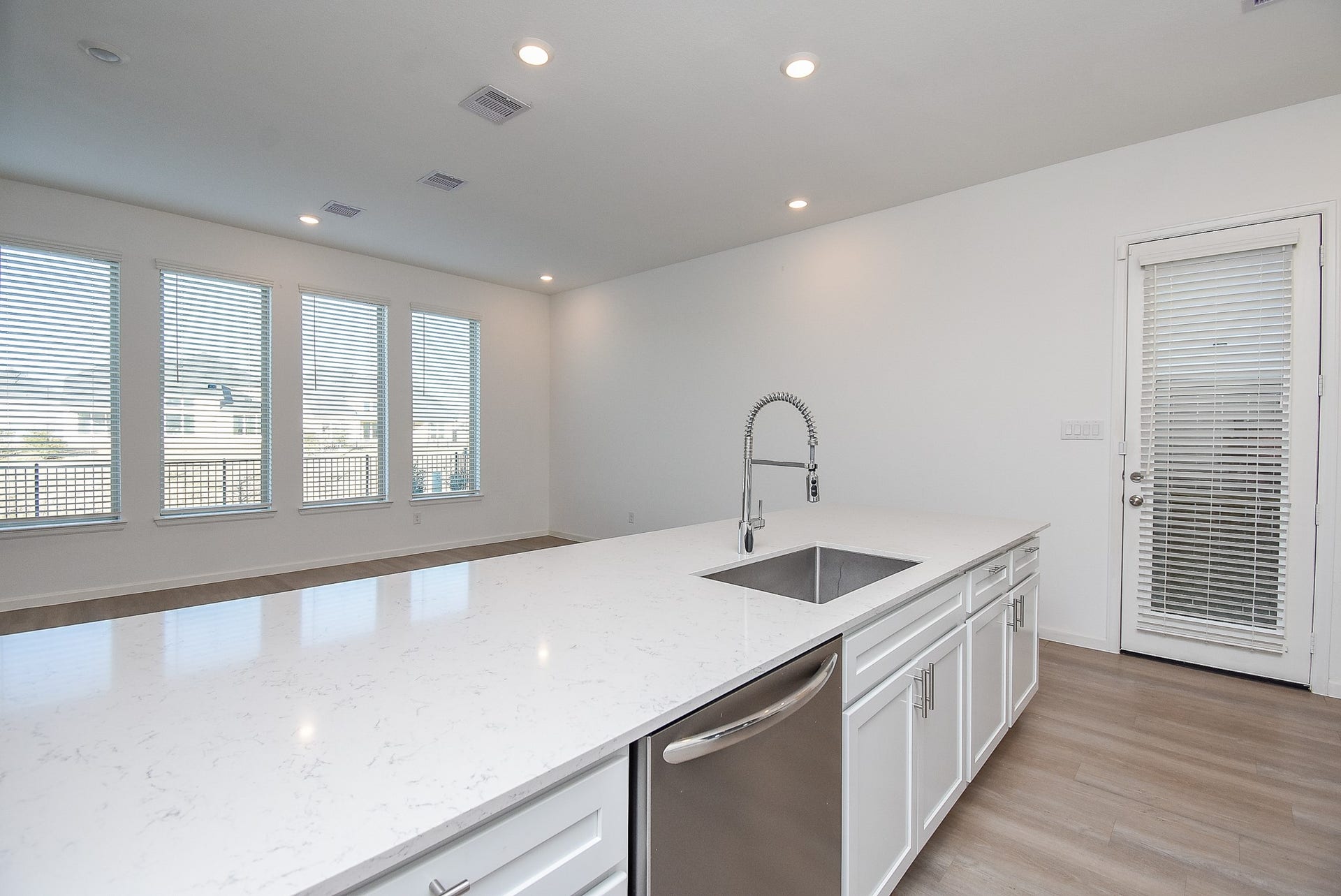 A large quartz island with a stainless steel dishwasher, deep sink, and high-arc pull-down faucet. The white drawers cabinets feature stylish hardware and are soft close. The door leads to the side and back yard.