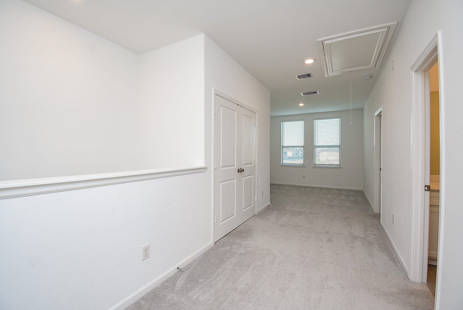 A bright upstairs hallway with neutral carpeting and white walls, leading to additional rooms and the flex space.