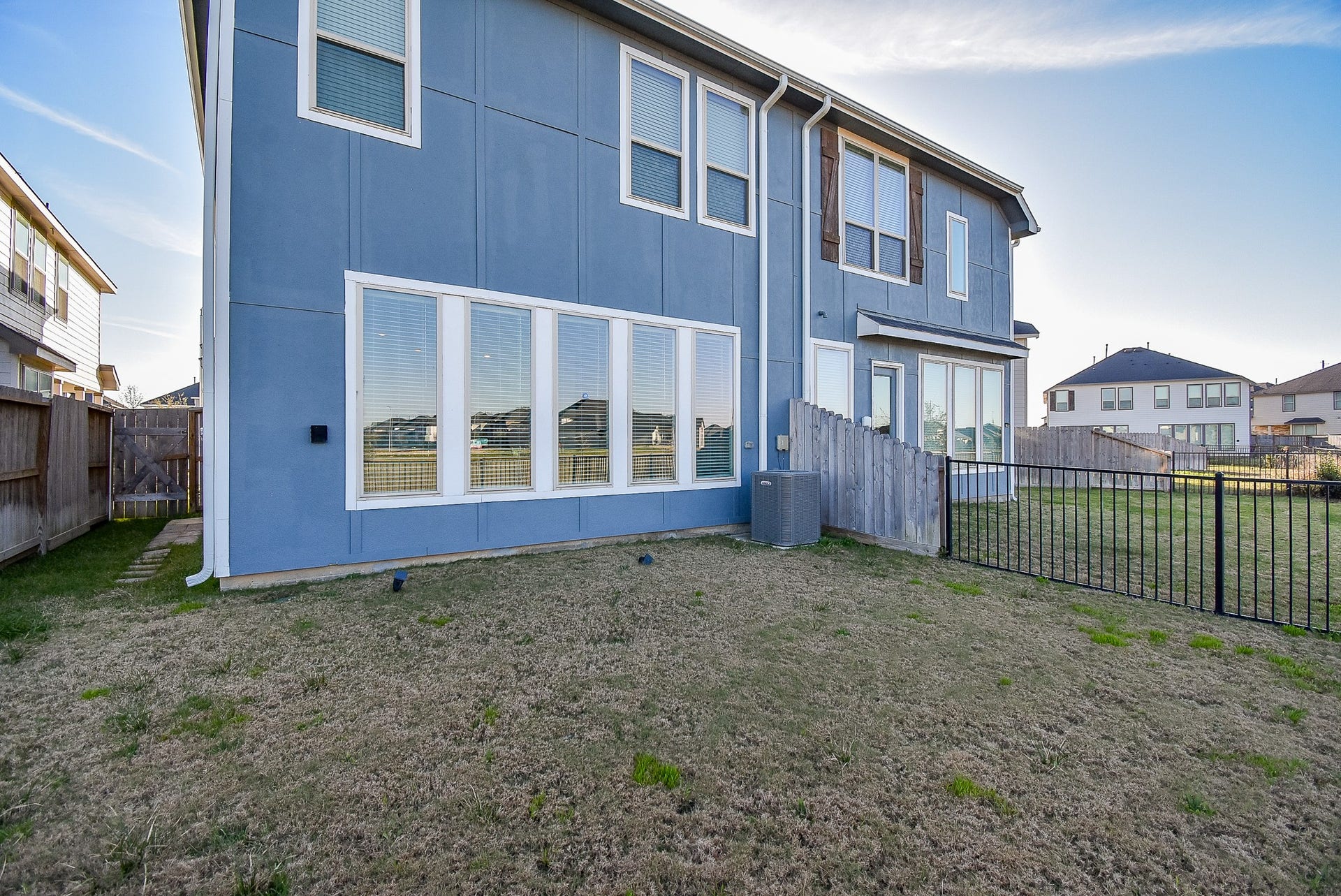 A rear exterior view of the home showing the gutters for additional irrigation control. The fenced yard offers a mix of wood and wrought iron fencing, providing both privacy and scenic views of the surrounding neighborhood. The side gate allows easy access to the backyard.