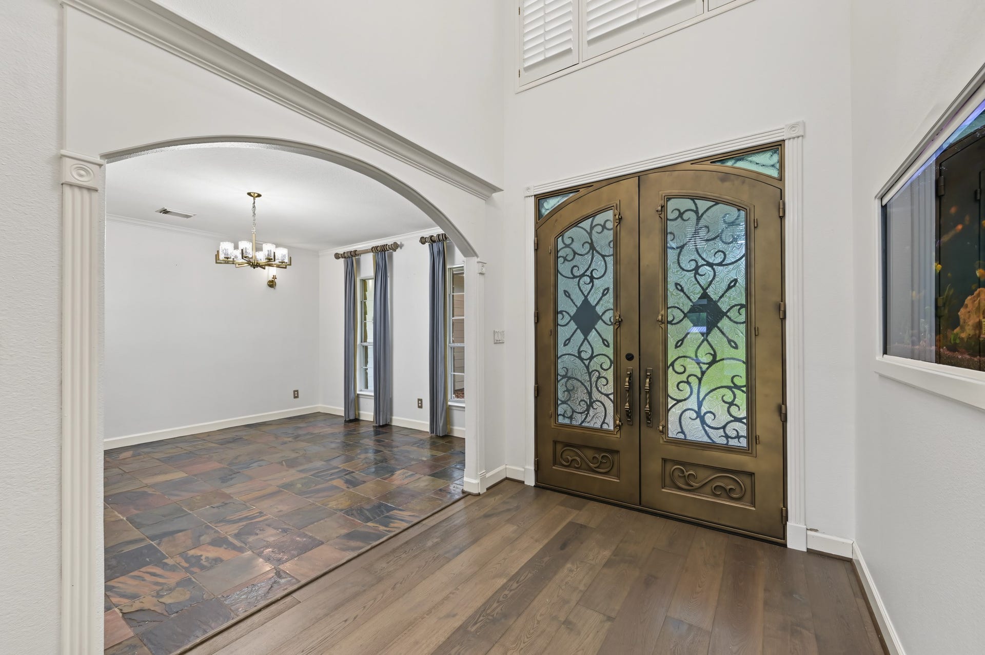 Elegant entryway with intricate double doors and a spacious dining area, featuring rich tile flooring and stylish lighting.