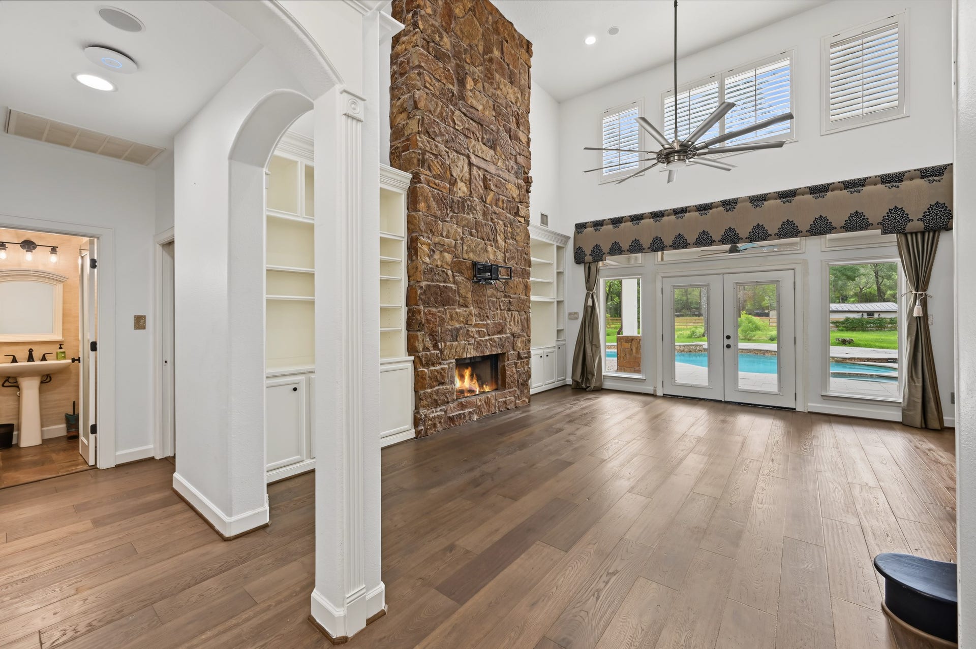Spacious living area featuring a stunning floor-to-ceiling stone fireplace, elegant hardwood floors, and large windows offering a view of the pool.