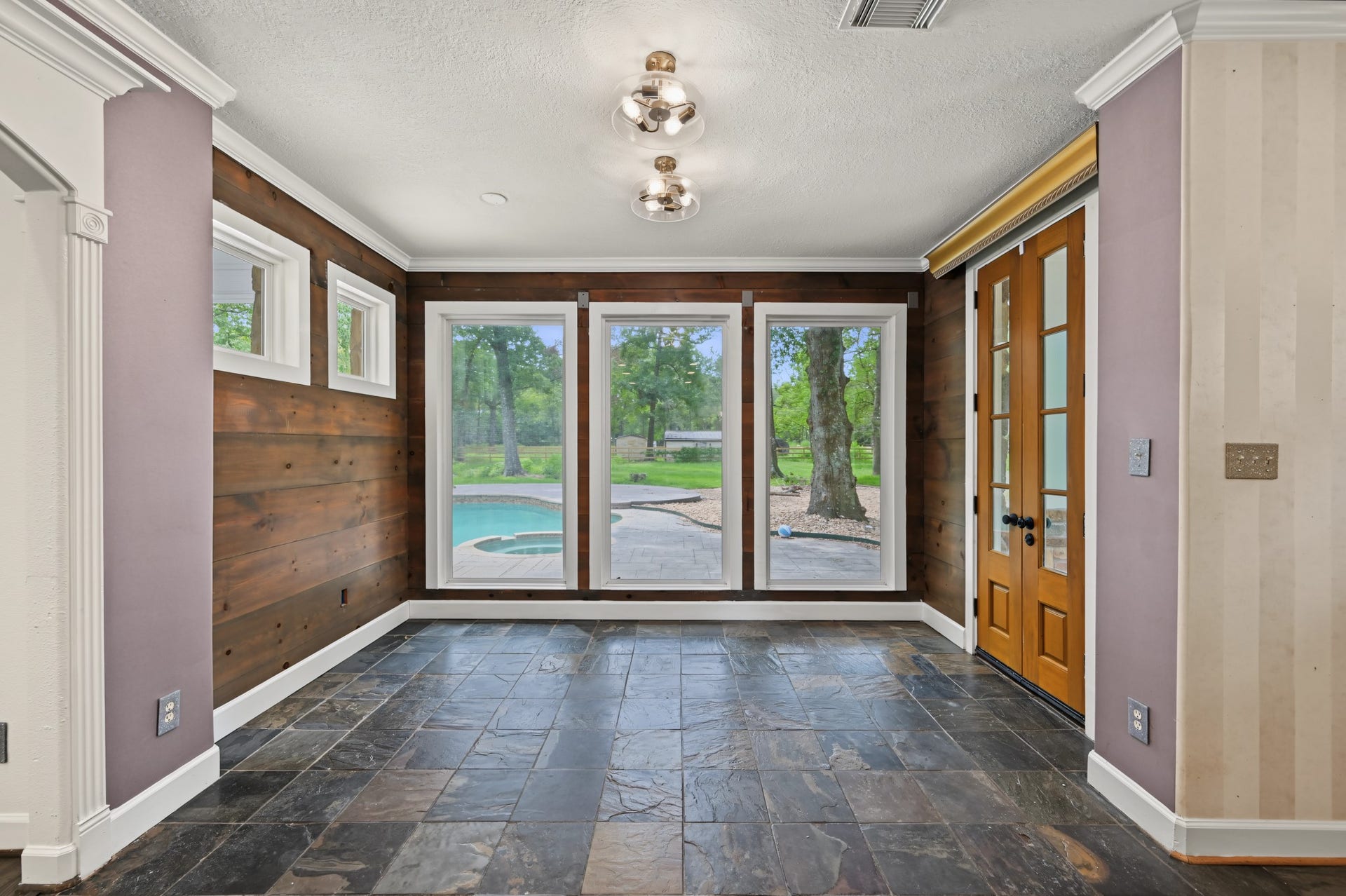 Bright and inviting breakfast nook with slate flooring, wood panel accents, and large windows offering a serene view of the backyard pool and lush greenery.
