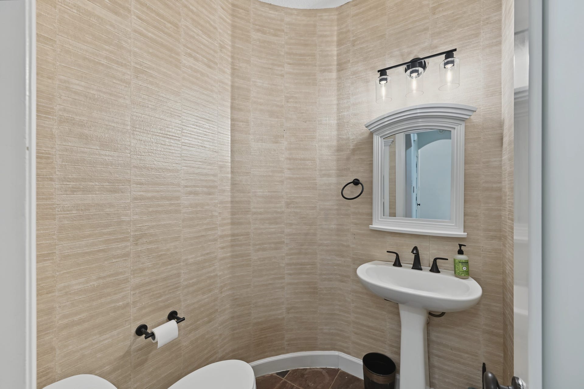 Charming half-bath with elegant wallpaper, featuring a pedestal sink, stylish mirror, and modern light fixtures.