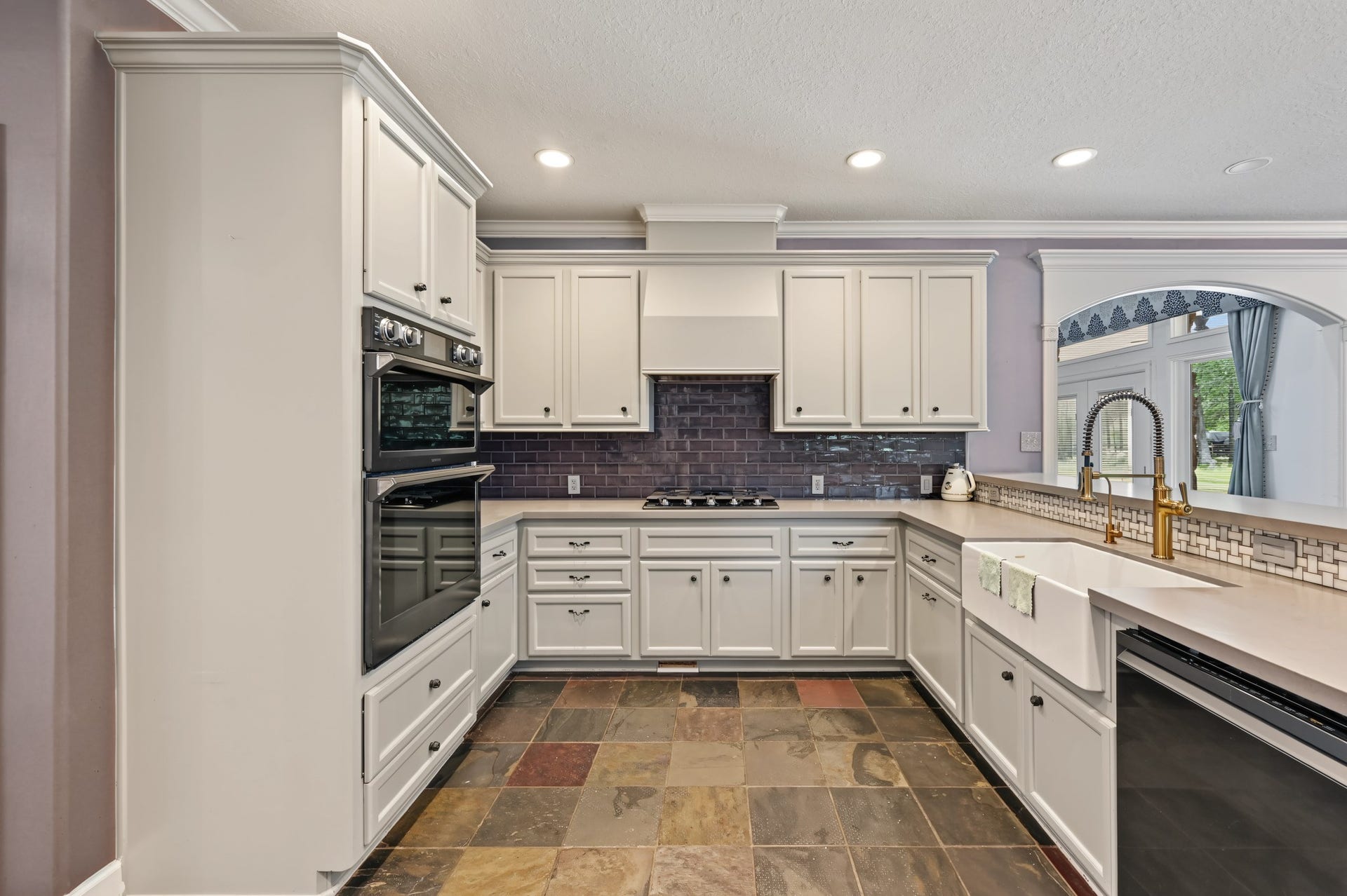 Elegant kitchen with modern appliances, sleek cabinetry, and a stylish tile backsplash. Features a spacious countertop with a farmhouse sink and ample natural light through large windows.