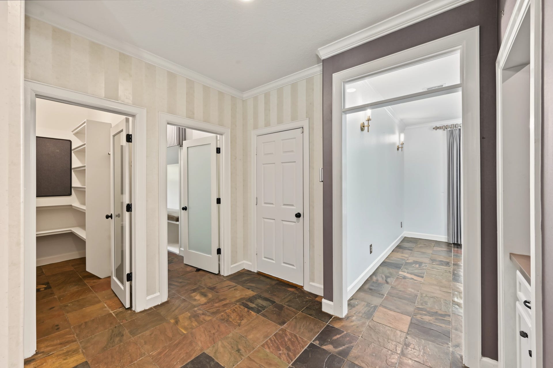 Spacious hallway features elegant slate flooring and multiple doorways, including a walk-in pantry with ample shelving and frosted glass doors.