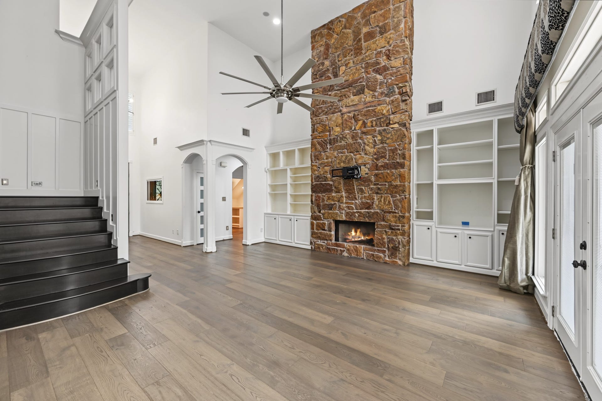Expansive living area featuring a stunning floor-to-ceiling stone fireplace, elegant built-in shelving, and abundant natural light from large windows.