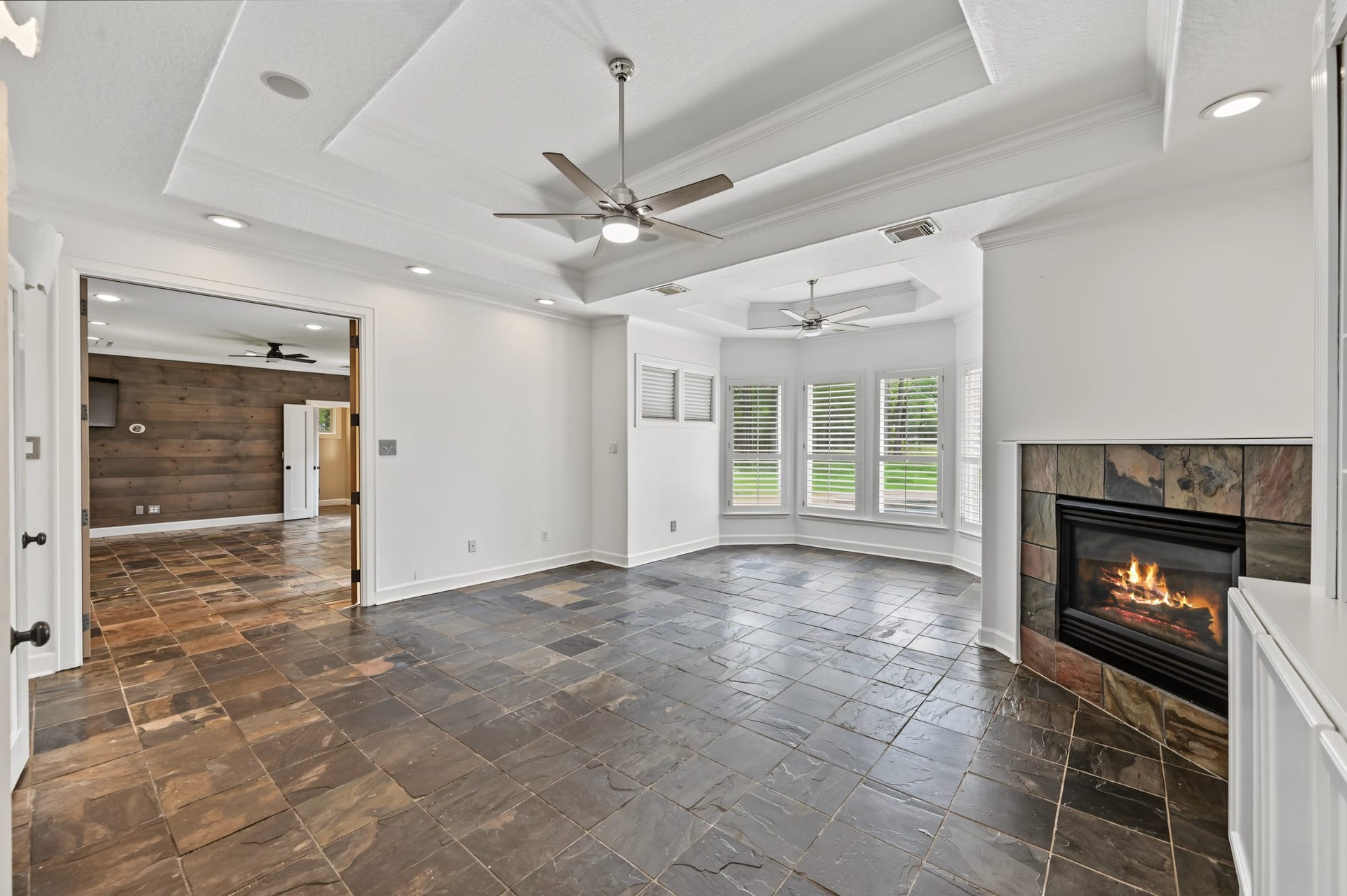 Experience the charm of this elegant primary bedroom space featuring a cozy fireplace, stylish slate flooring, and abundant natural light from the bay windows.