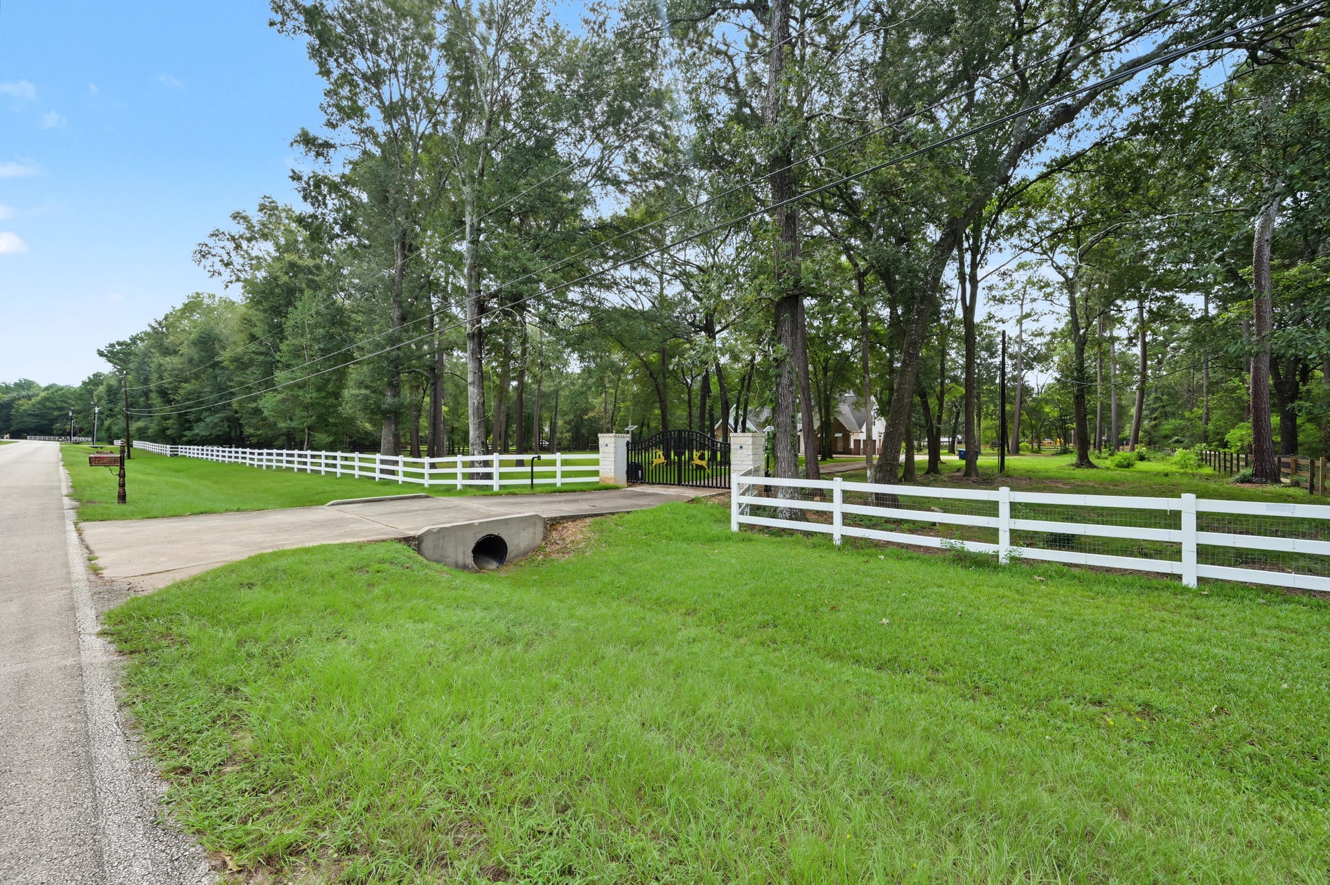 Charming country estate with a white picket fence, tree-lined driveway, and expansive green lawns, offering a serene and private retreat.