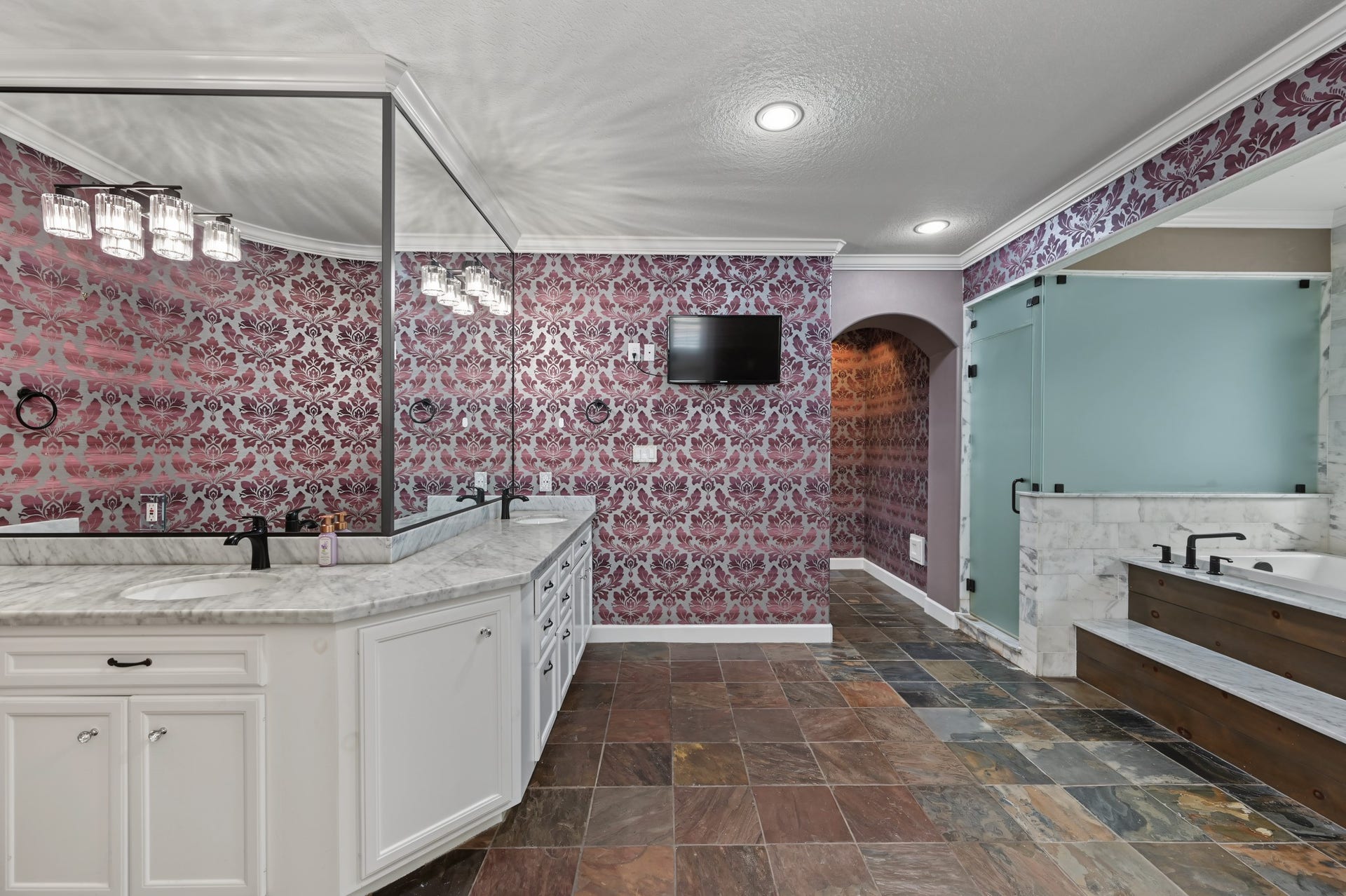 Luxurious bathroom featuring elegant floral wallpaper, a large vanity with dual sinks, spacious walk-in shower with frosted glass, massive sepearte spa like tub to soak after a long day!