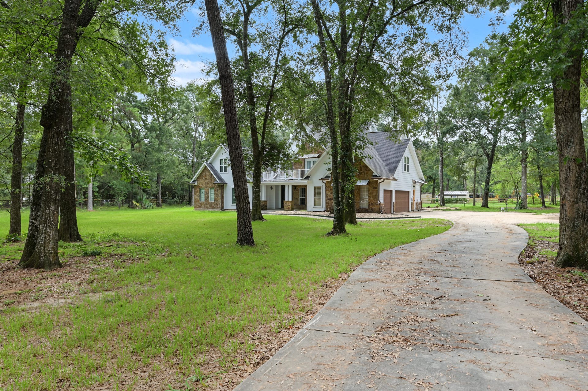 Home is nestled among mature trees with a winding driveway  leading to a picturesque front entrance.