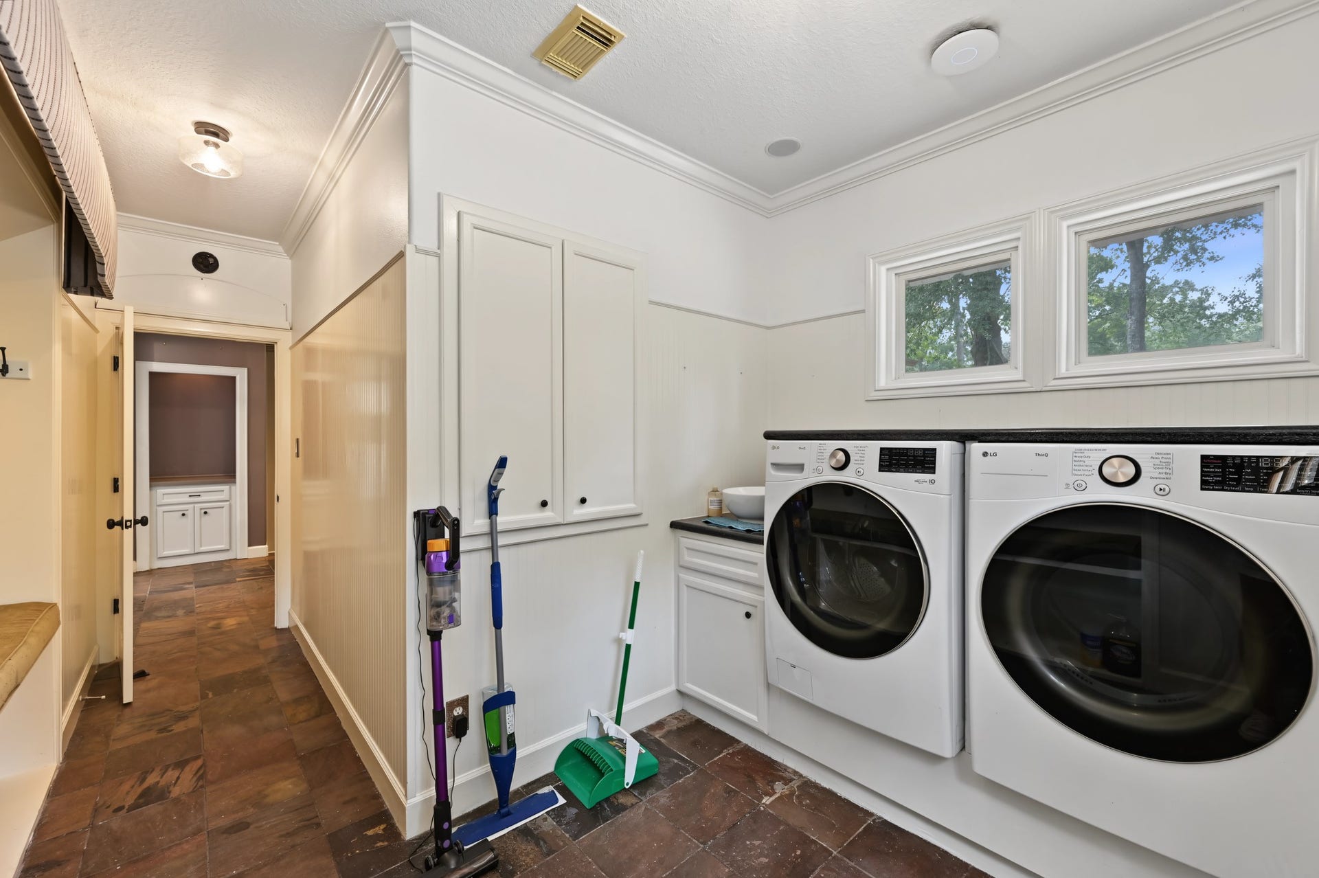 Spacious laundry room featuring modern front-loading washer and dryer, ample cabinetry, and natural light from two large windows and a sink!