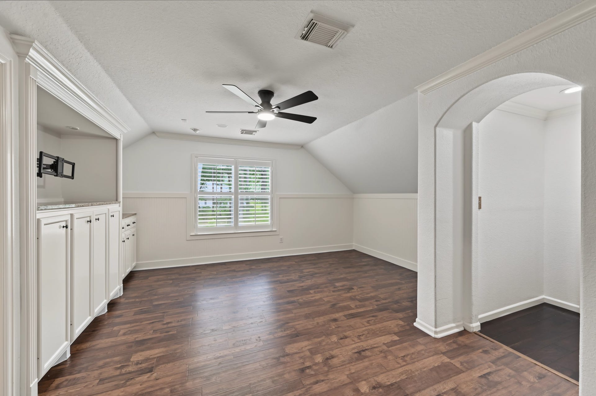 Bright and spacious room with elegant wood flooring, built-in cabinetry, and a modern ceiling fan, perfect for a cozy retreat or entertainment space.