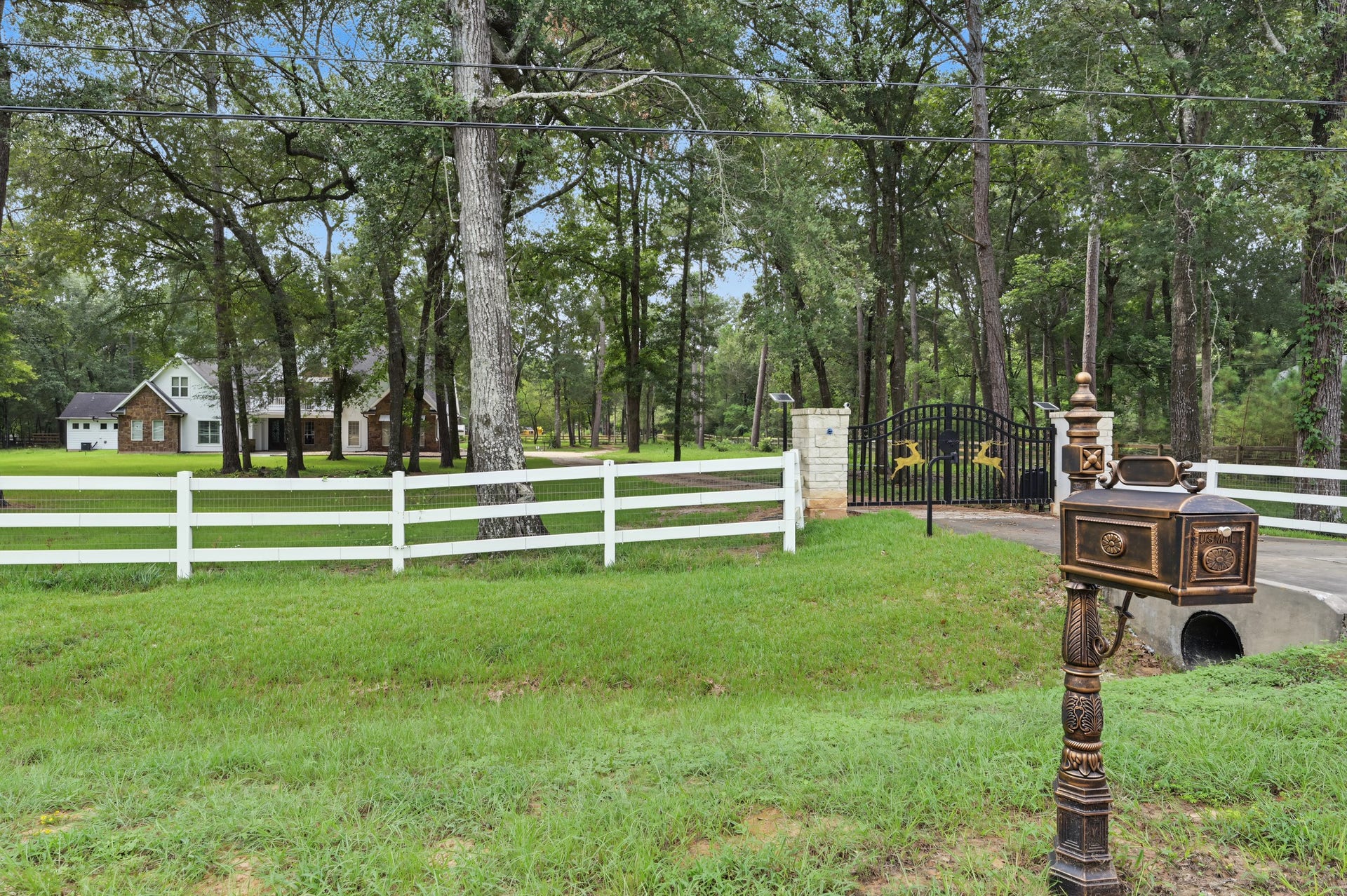 Charming home set amidst lush greenery, featuring a welcoming gated entrance and classic white fencing for added privacy and elegance.
