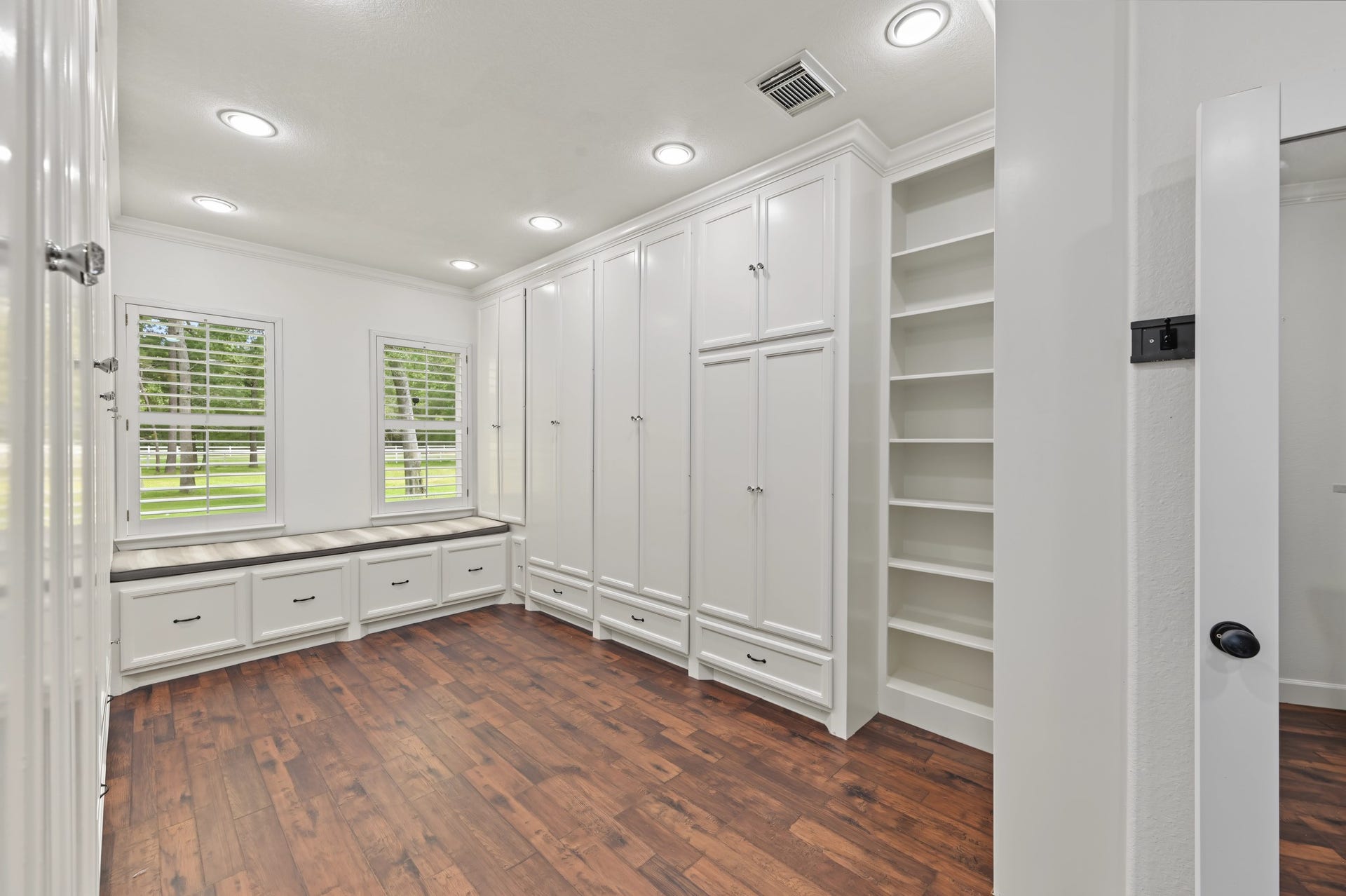 Spacious walk-in closet featuring custom built-in cabinetry, abundant shelving, and large windows for natural light, complemented by elegant wood flooring. Also a hidden storage behind the glass mirror!