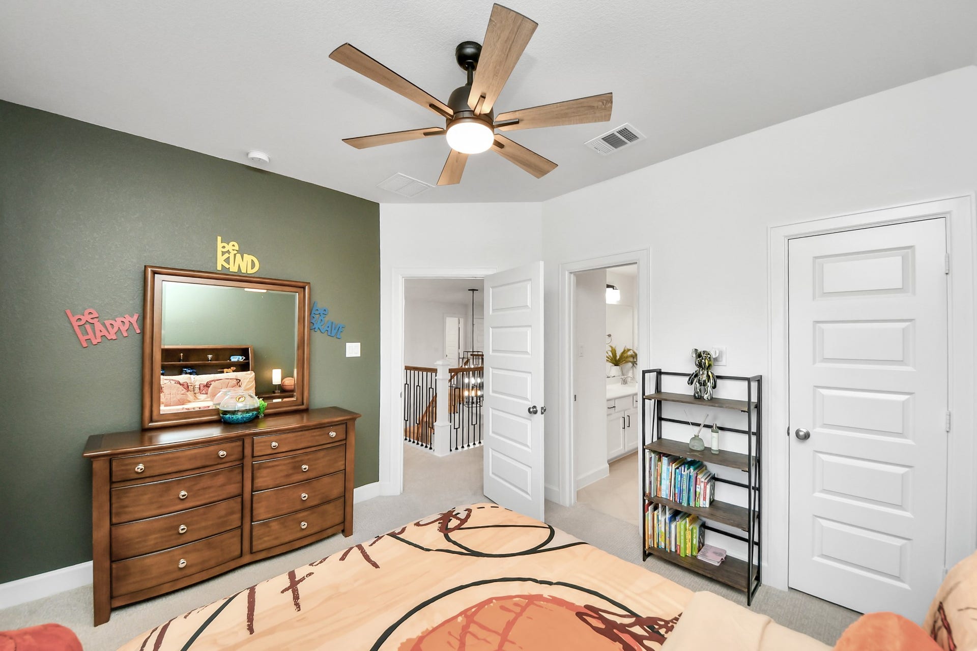 5542 Fairfield Lane, Pasadena, TX 77505 Cozy bedroom with a stylish green accent wall, modern ceiling fan, and ample natural light. Features a wooden dresser with a mirror, open shelving for books and decor, and access to a well-lit bathroom.