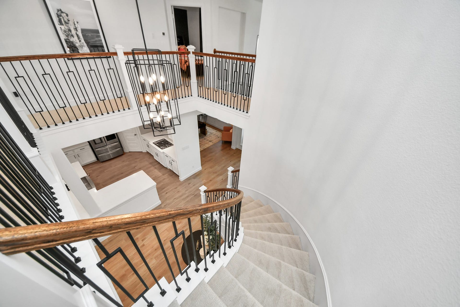5542 Fairfield Lane, Pasadena, TX 77505 Elegant curved staircase with wrought iron railings leads to an open upper landing, overlooking a modern kitchen with sleek appliances and hardwood floors.
