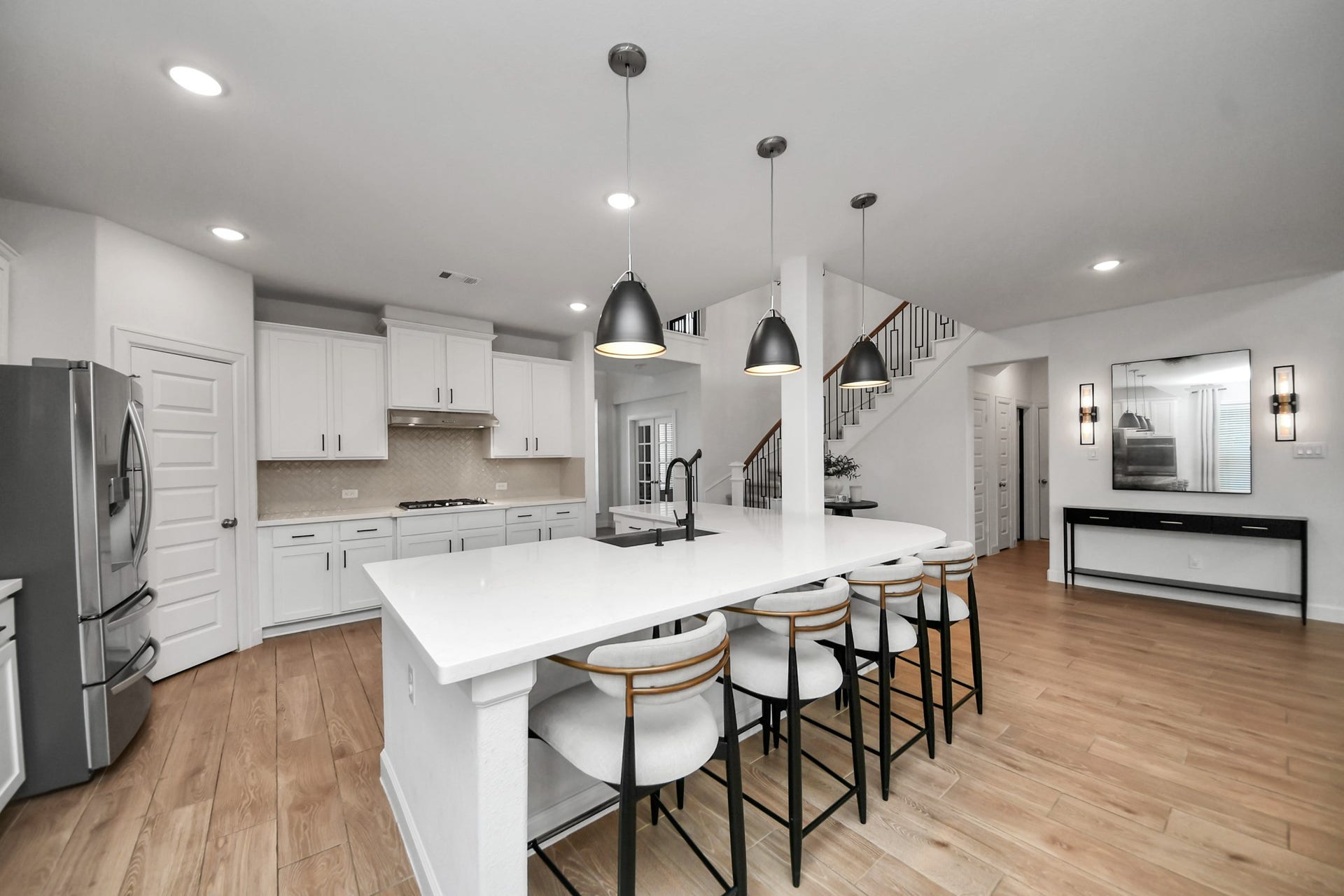 5542 Fairfield Lane, Pasadena, TX 77505 Spacious and modern kitchen with sleek white cabinetry, a large center island with seating, stainless steel appliances, and elegant pendant lighting, seamlessly flowing into an open living area with a stylish staircase.