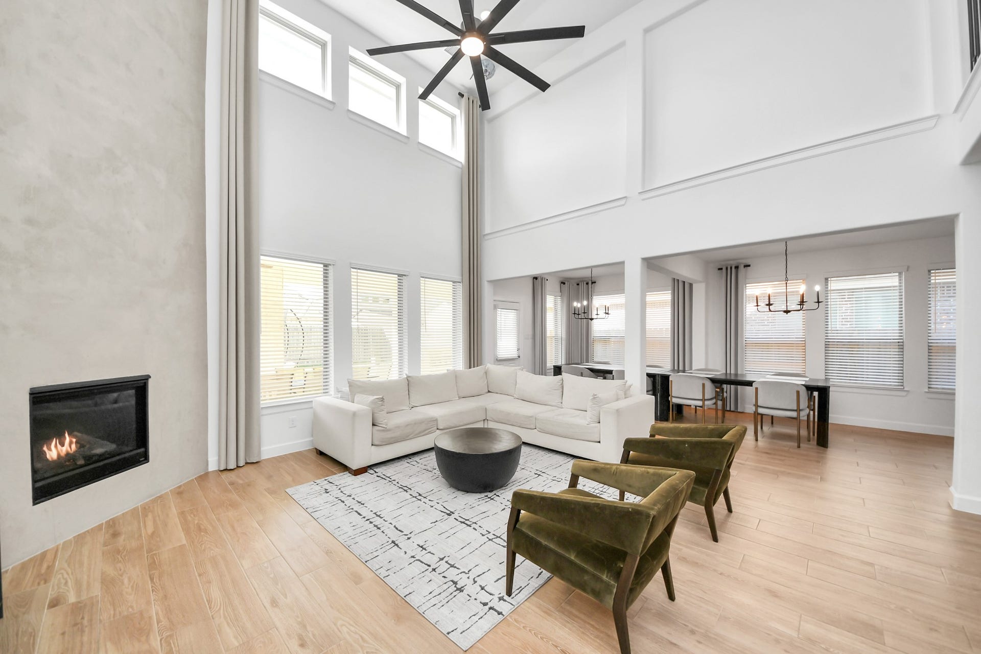 5542 Fairfield Lane, Pasadena, TX 77505 Stunning two-story living area features a cozy fireplace, expansive windows for abundant natural light, custom two-story curtains, and elegant hardwood floors, seamlessly connecting to a stylish dining space.