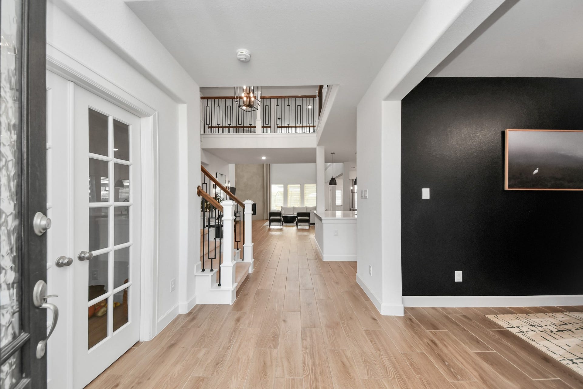 5542 Fairfield Lane, Pasadena, TX 77505 Elegant front entrance view with sleek wood flooring, French doors, and a view into the spacious, open-plan living area featuring a modern staircase and stylish black accent wall.