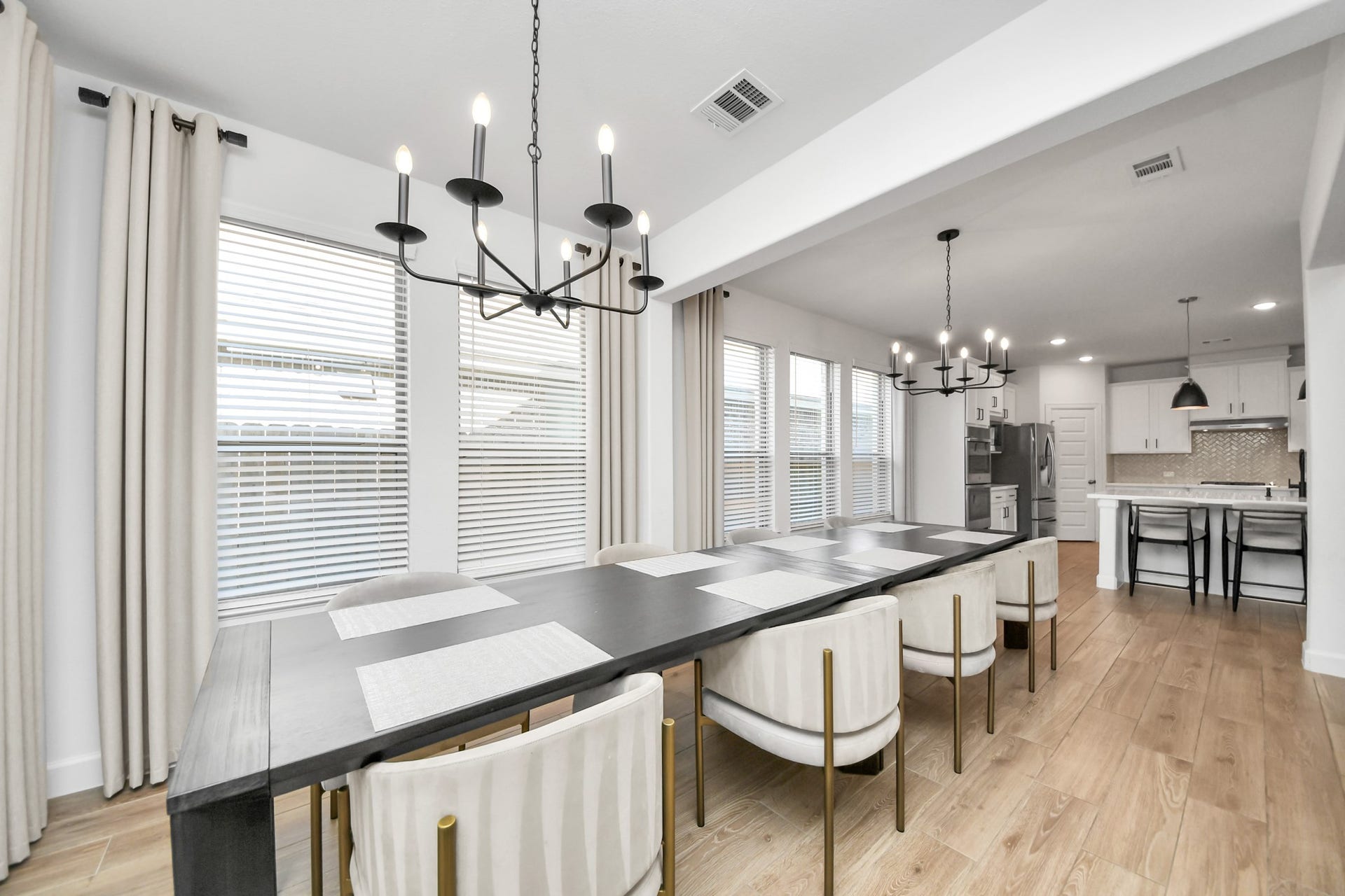 5542 Fairfield Lane, Pasadena, TX 77505 Elegant dining area with a long table, modern chandelier, and large windows offering abundant natural light, seamlessly flowing into a sleek kitchen with stainless steel appliances.