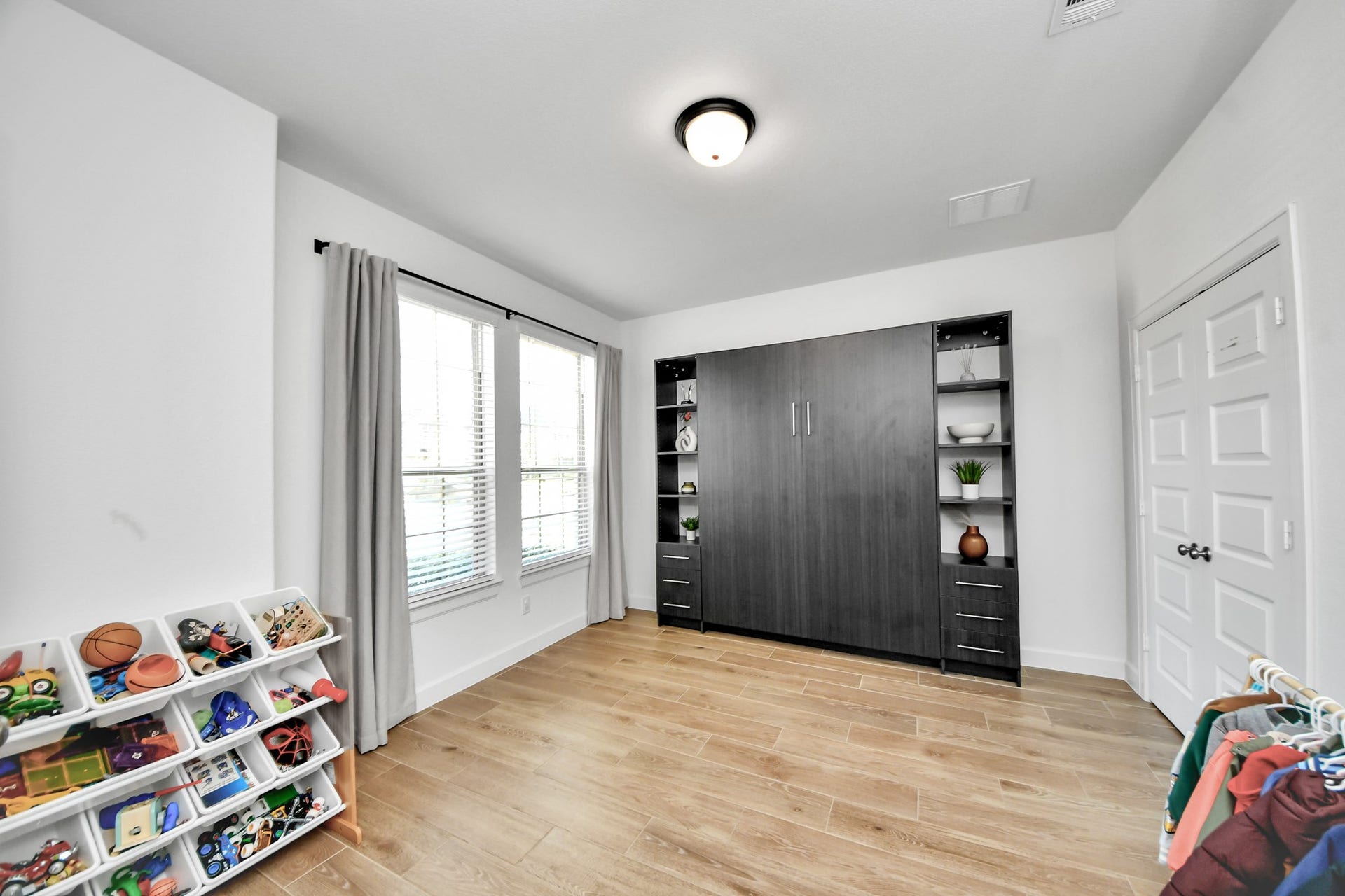 5542 Fairfield Lane, Pasadena, TX 77505 Bright and versatile room featuring a built-in Murphy bed with shelving, large window for natural light, and stylish wood flooring, perfect for a guest room or play area.