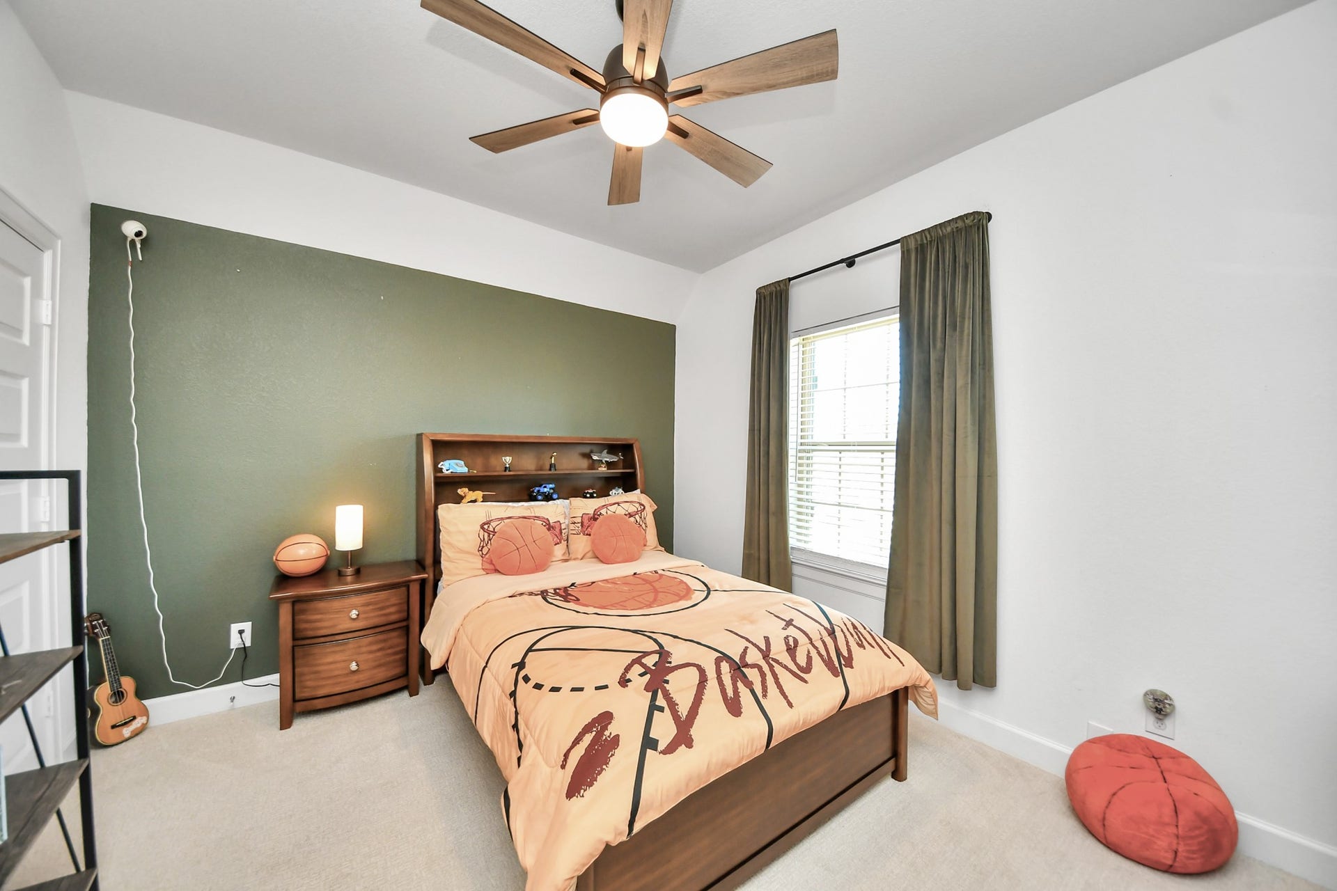 5542 Fairfield Lane, Pasadena, TX 77505 Cozy bedroom featuring a basketball-themed decor, accentuated by a warm green accent wall and ample natural light from a large window.