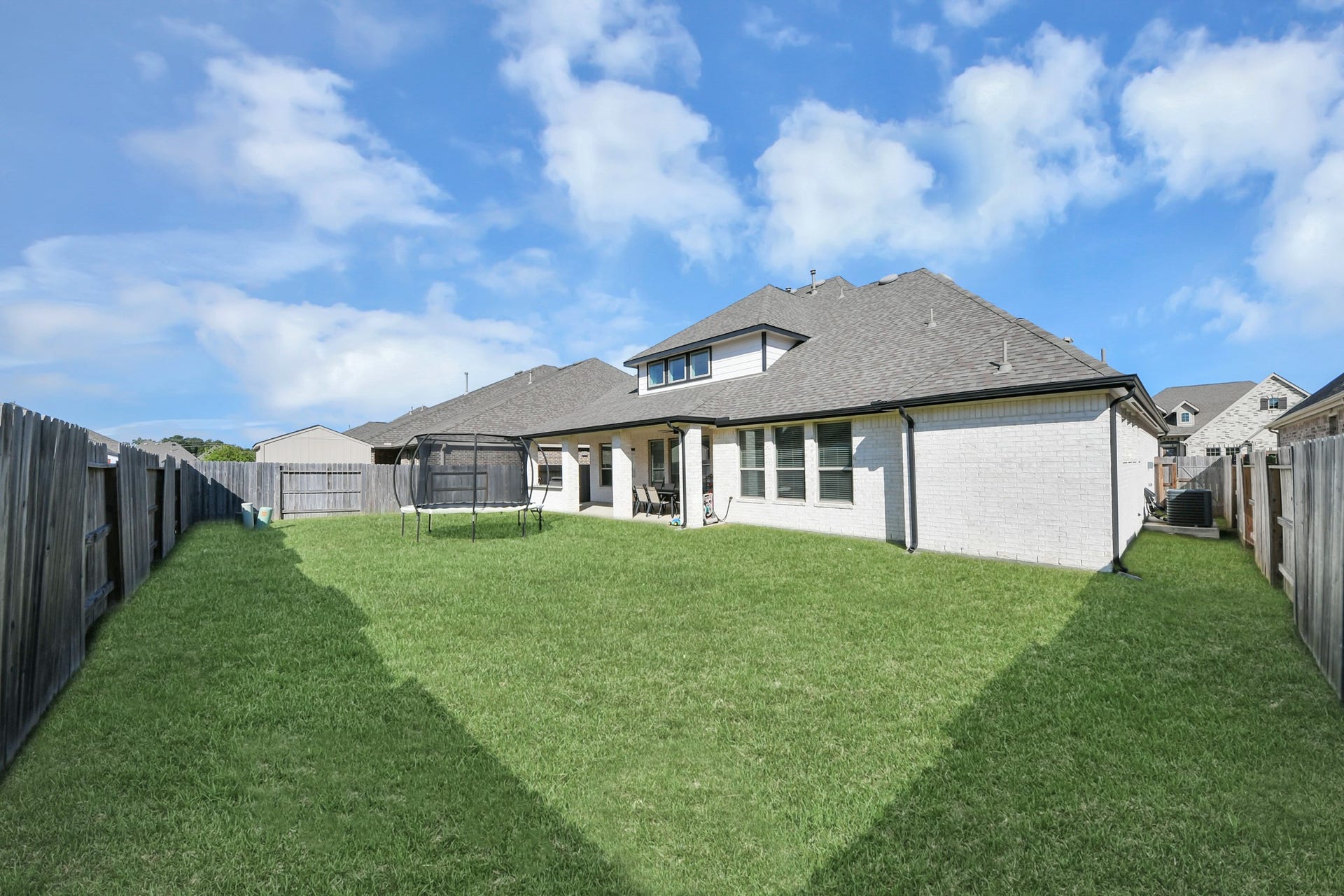 5542 Fairfield Lane, Pasadena, TX 77505 Spacious fenced backyard with lush green grass and a covered patio, perfect for outdoor activities and relaxation.