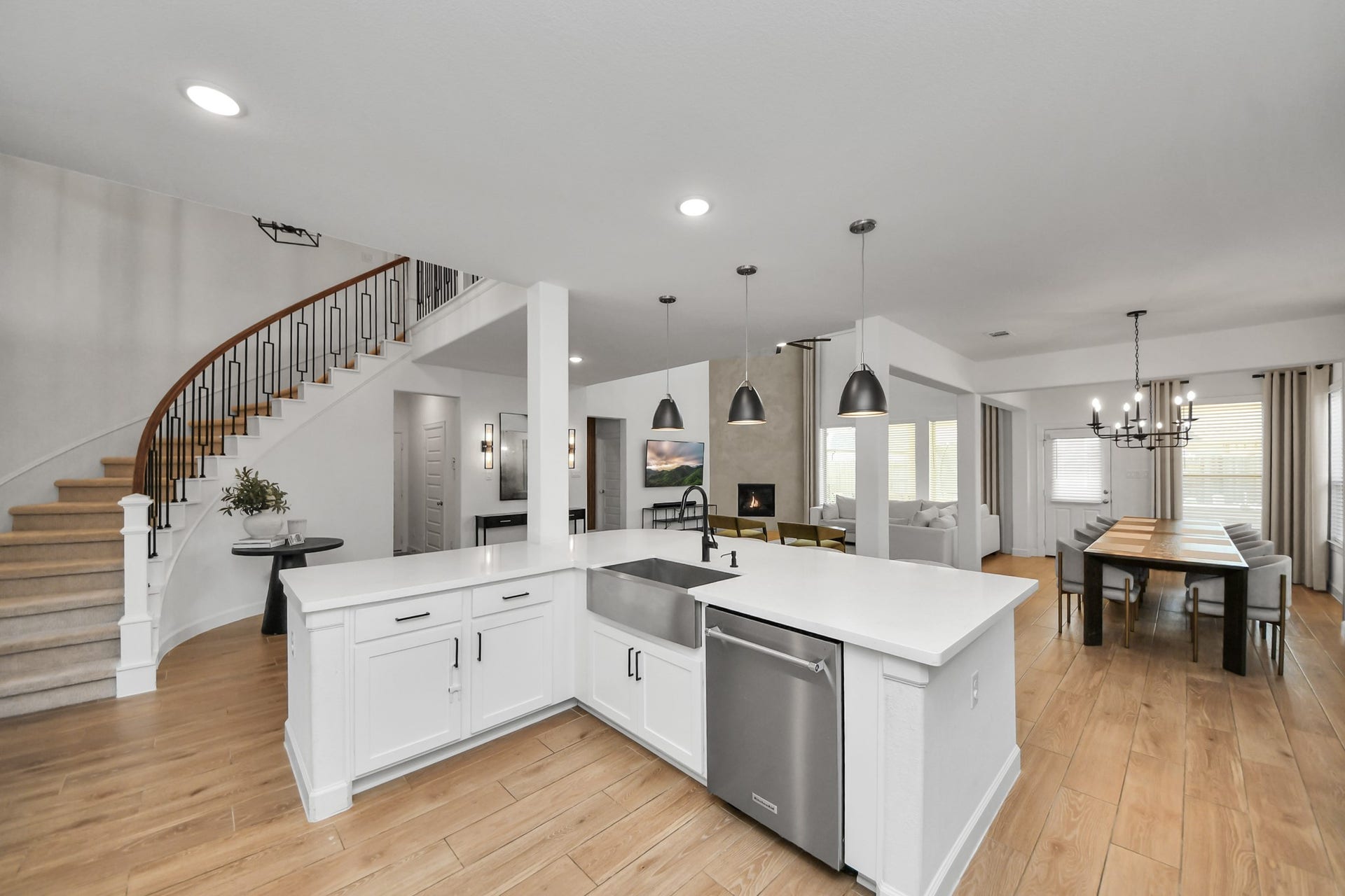 5542 Fairfield Lane, Pasadena, TX 77505 Elegant open-concept kitchen and dining area featuring sleek white cabinetry, modern pendant lighting, and a sweeping staircase, seamlessly connecting to a cozy living space with a fireplace.