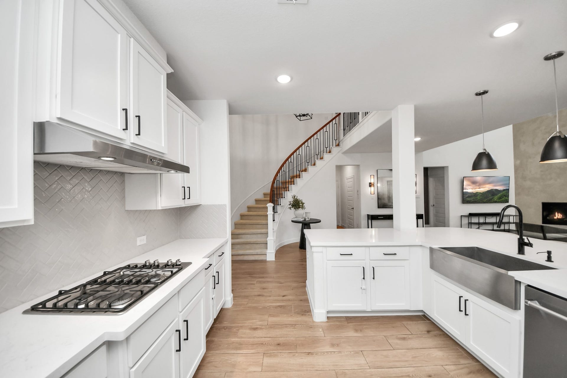 5542 Fairfield Lane, Pasadena, TX 77505 Spacious kitchen with sleek white cabinetry, a modern gas cooktop, and an elegant herringbone backsplash. The open layout flows seamlessly into the living area, highlighted by a curved staircase and warm wood flooring.