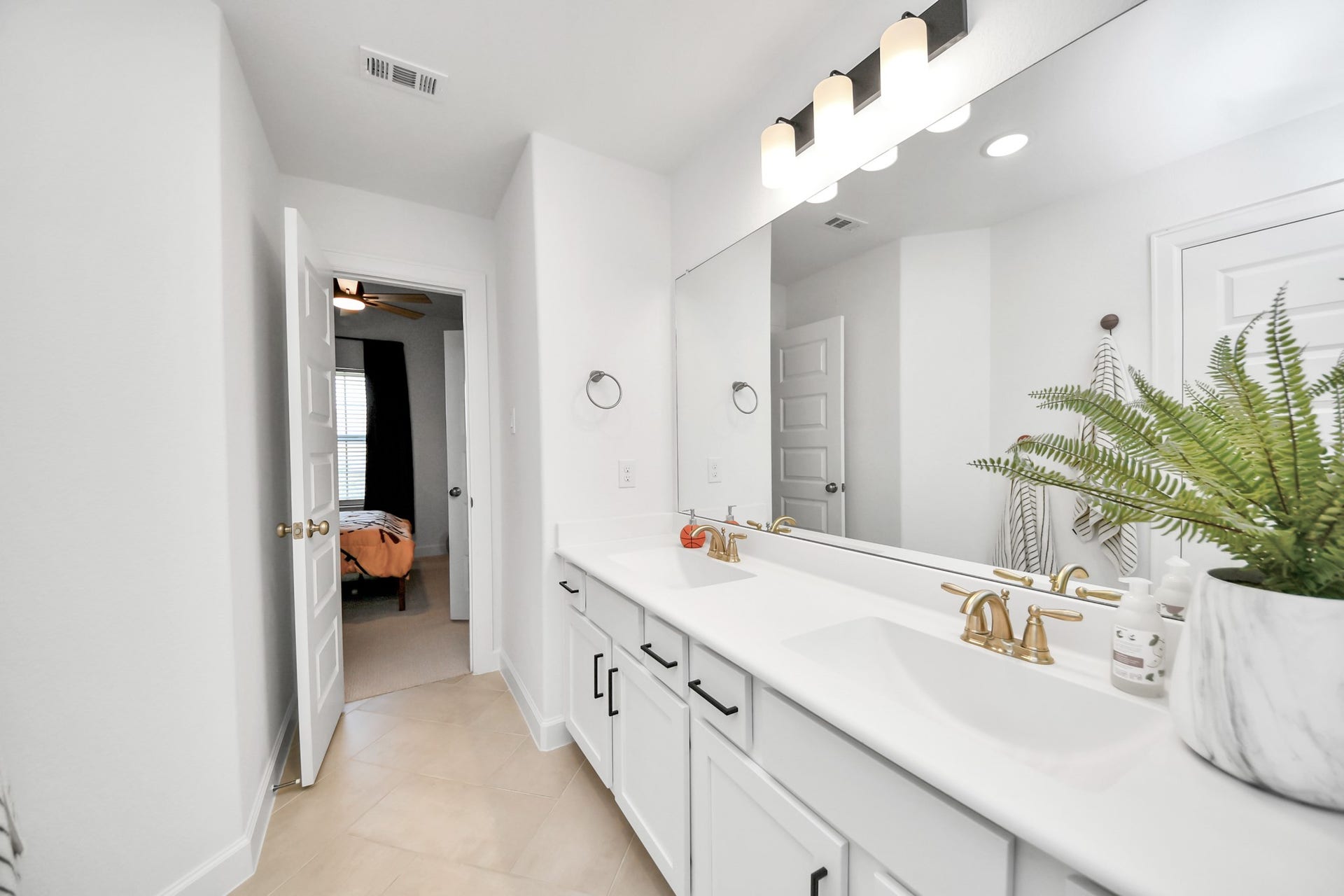 5542 Fairfield Lane, Pasadena, TX 77505 Bright and modern Jack and Jill bathroom featuring a double vanity with sleek gold fixtures, a large mirror, and ample storage, leading into a cozy bedroom.