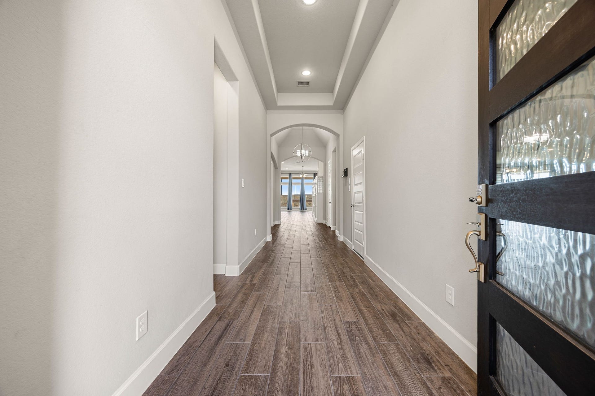 A grand first impression awaits as you step through the beautiful glass-paneled front door. An extended entryway draws you in with soaring 12-foot tray ceilings, recessed lighting, and elegant wood-look tile flooring that guides you effortlessly into the heart of the home.