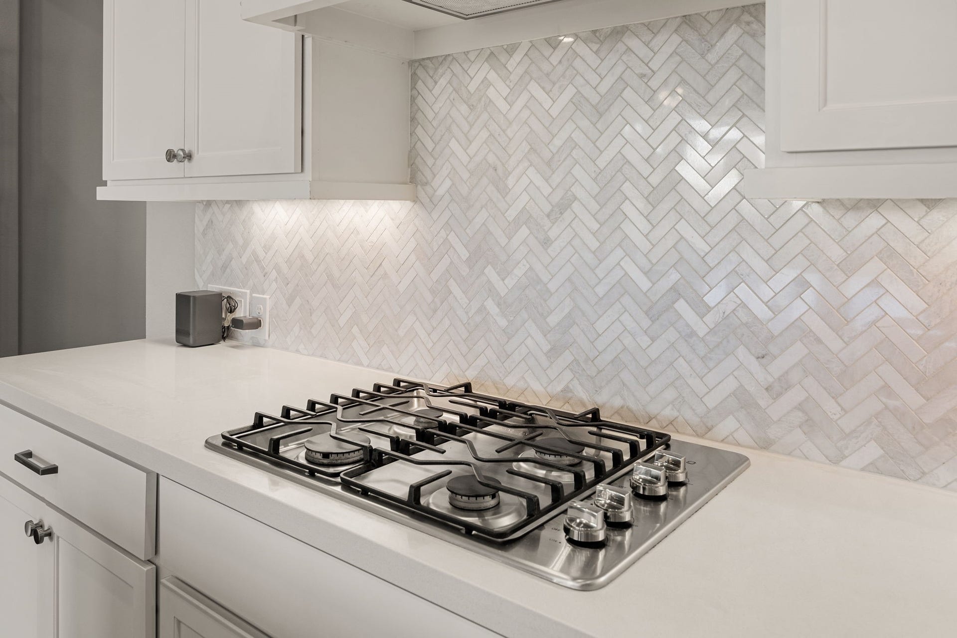 Attention to detail shines in this culinary corner, featuring a premium five-burner gas cooktop integrated seamlessly into the quartz countertops. A striking marble herringbone backsplash serves as a gorgeous focal point, beautifully highlighted by custom under-cabinet task lighting.