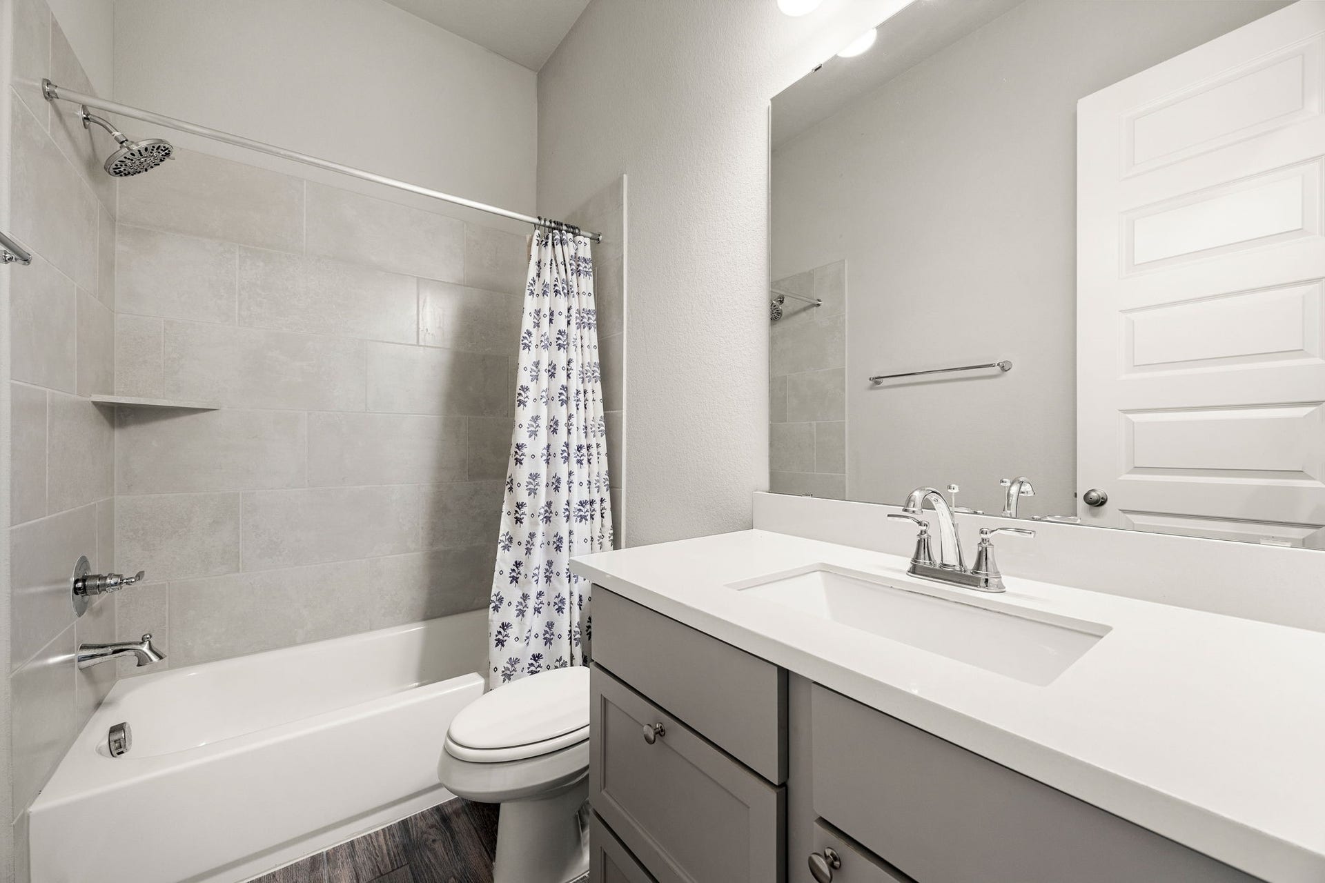 The pristine secondary bathroom features a stylish gray vanity with a crisp white undermount sink and a smooth engineered countertop. Perfect for family or guests, the space includes a full tub/shower combination beautifully finished with large-format tile surround that stretches to the ceiling, all tied together by durable wood-look flooring.