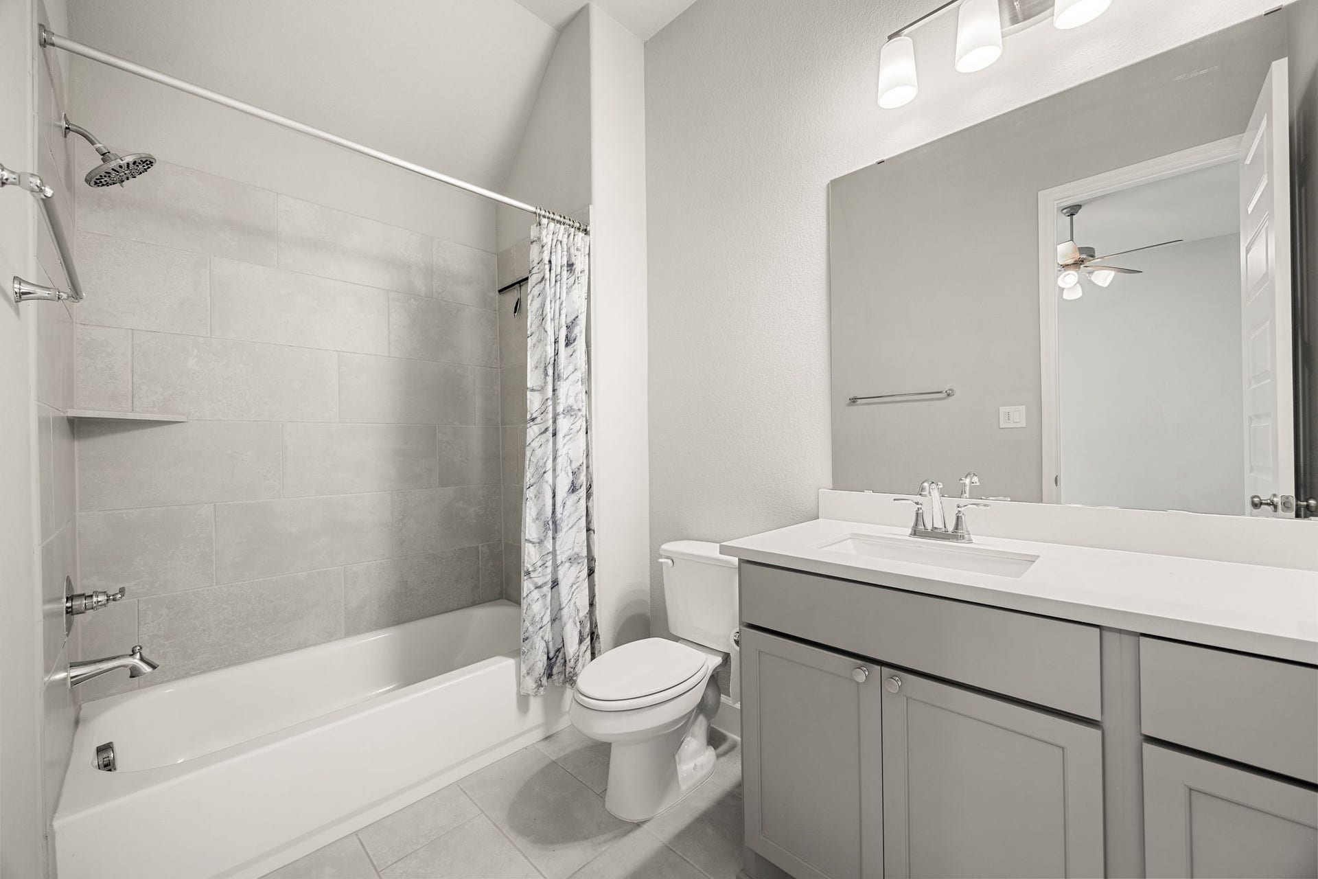The private en-suite bathroom offers true convenience for guests or family, featuring a modern gray vanity paired with a crisp white undermount sink. A classic tub/shower combination is elevated by a beautiful, neutral tile surround that extends high up the wall, perfectly accentuating the room's unique sloped ceiling architecture.