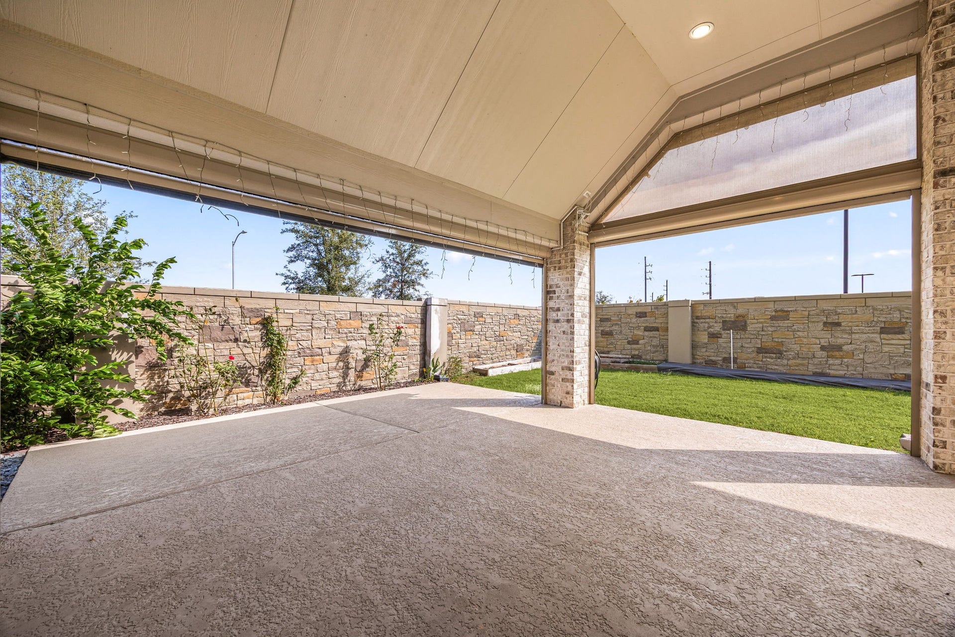 Step outside into your private retreat featuring an expansive extended covered patio with a dramatic high vaulted ceiling and integrated recessed lighting. The large concrete deck is finished with a durable, premium textured coating, looking out onto a perfectly manicured lawn enclosed by a beautiful engineered stone privacy wall with absolutely no rear neighbors.